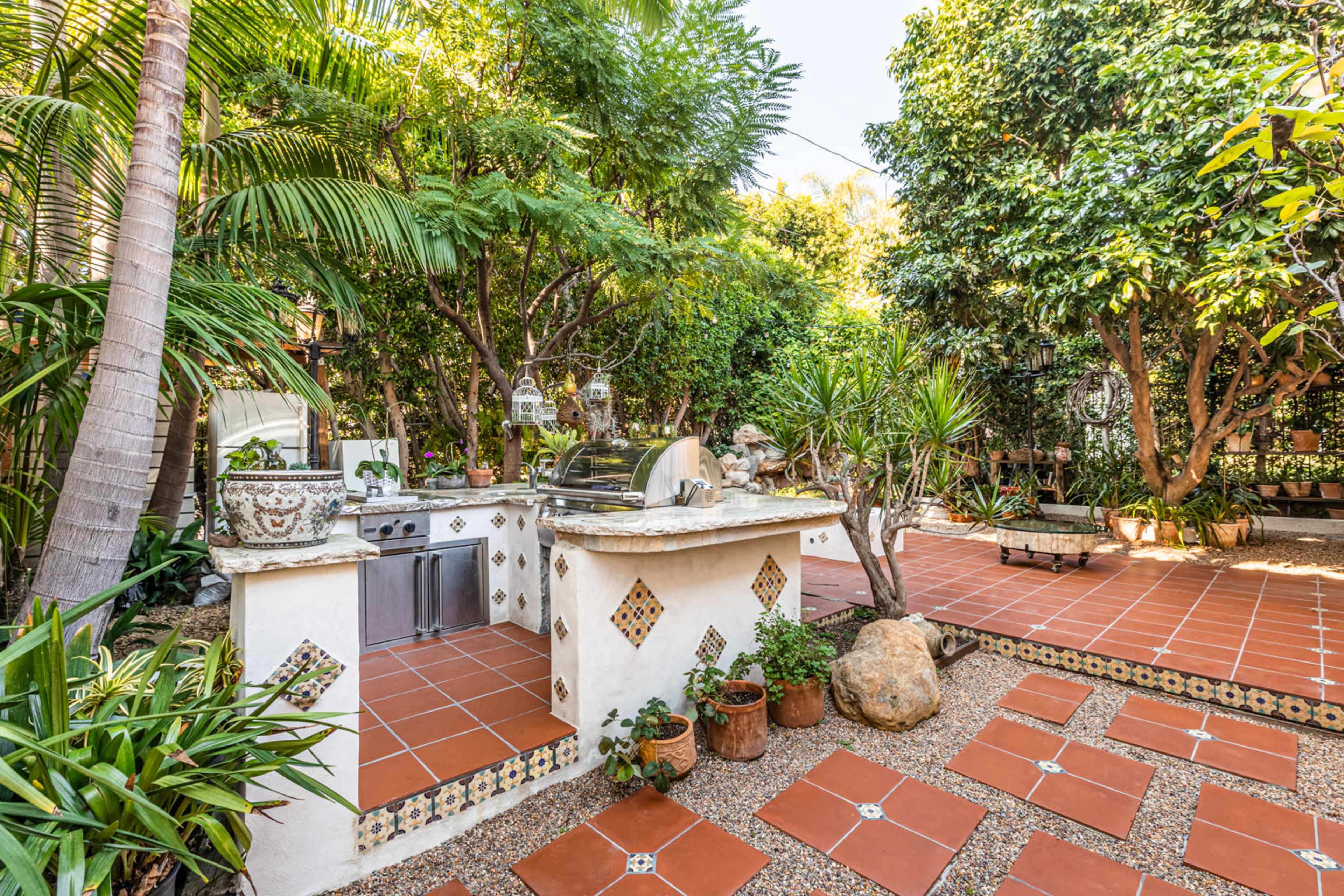 An outdoor kitchen area surrounded by lush greenery and stone pathways.