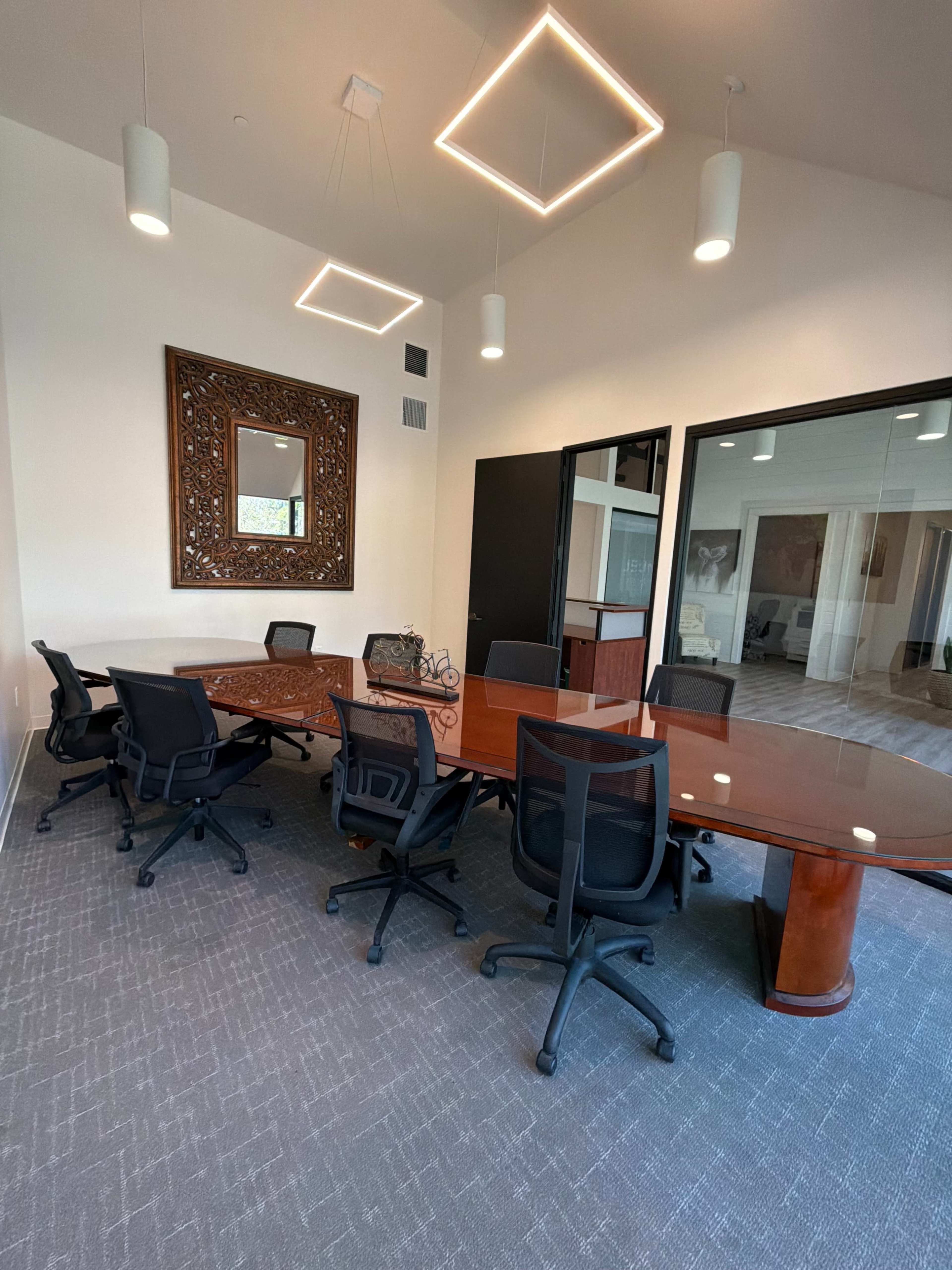 The image shows a modern conference room with a large wooden table surrounded by black chairs and illuminated by geometric pendant lights.
