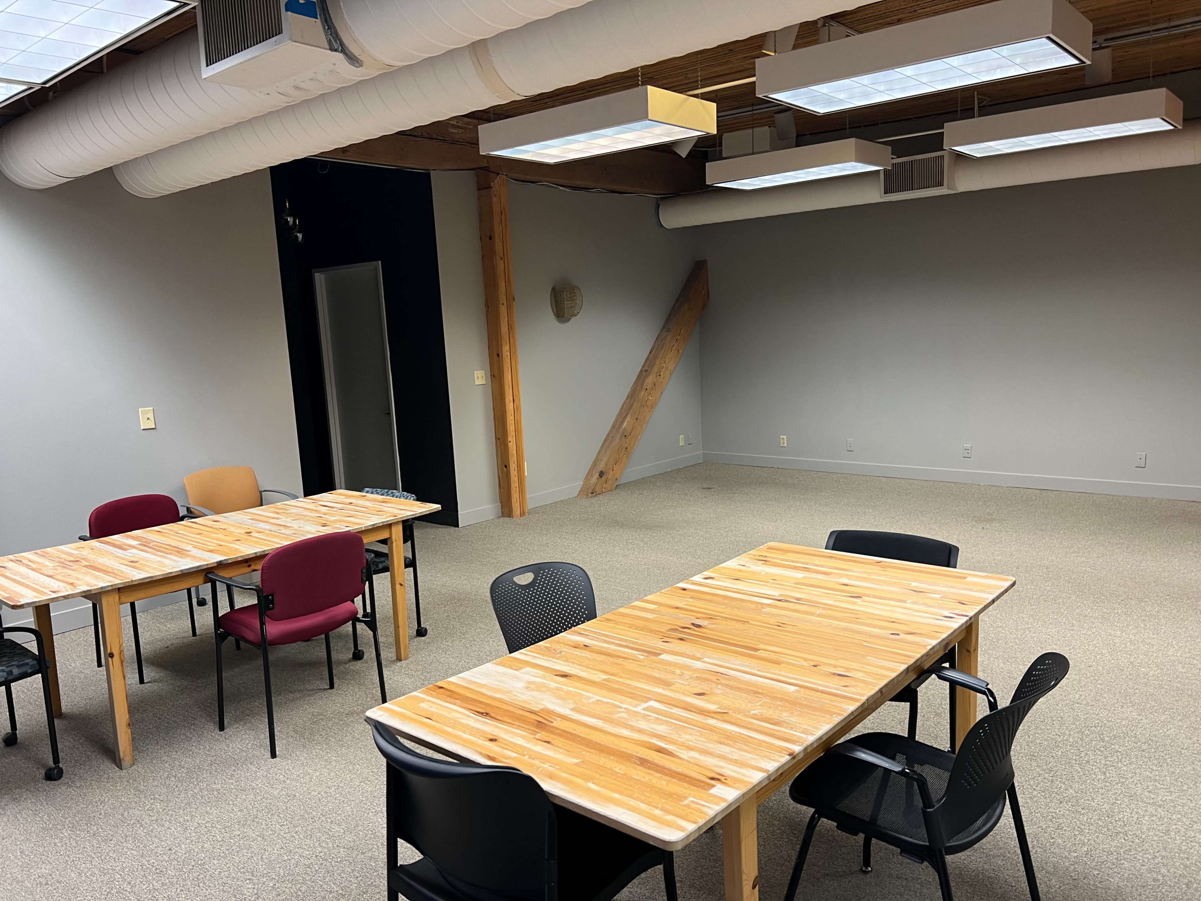 A spacious, unfurnished meeting room features several wooden tables and chairs arranged in a casual layout.