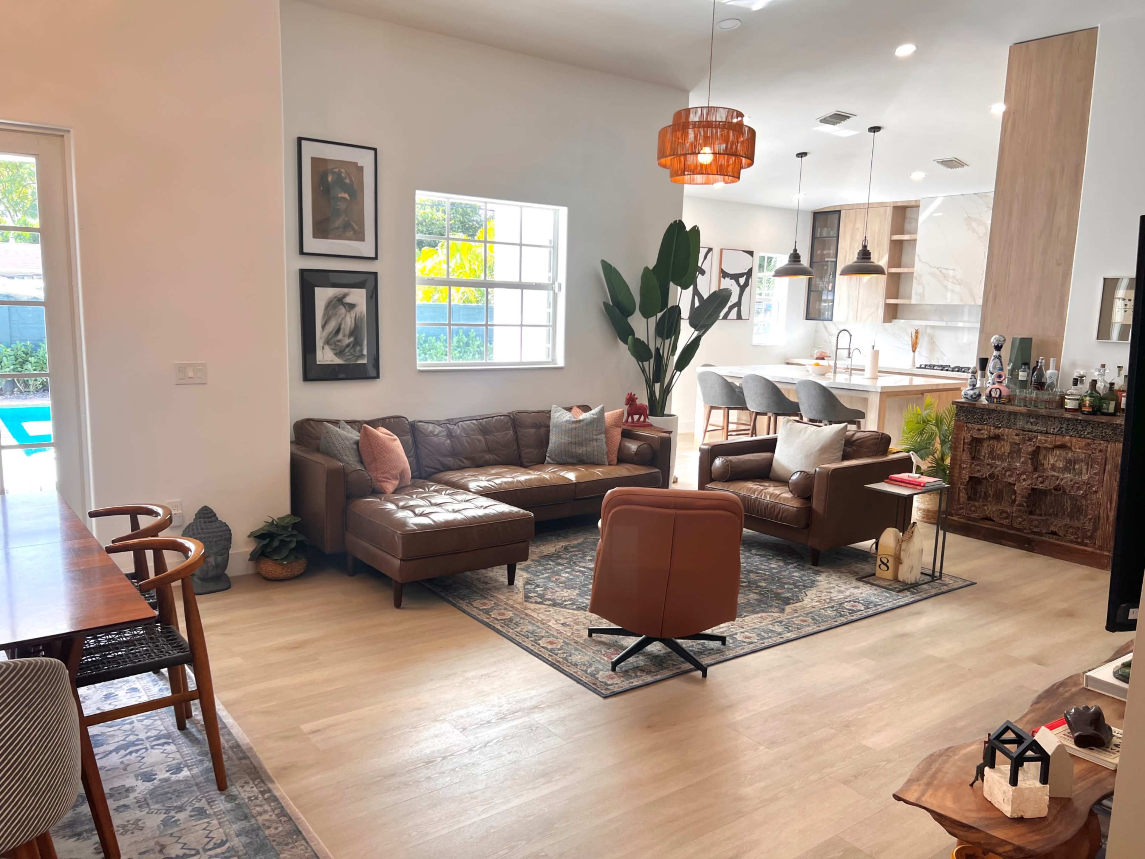A modern living space with leather furniture, a dining area, and large windows that open to a pool outside.