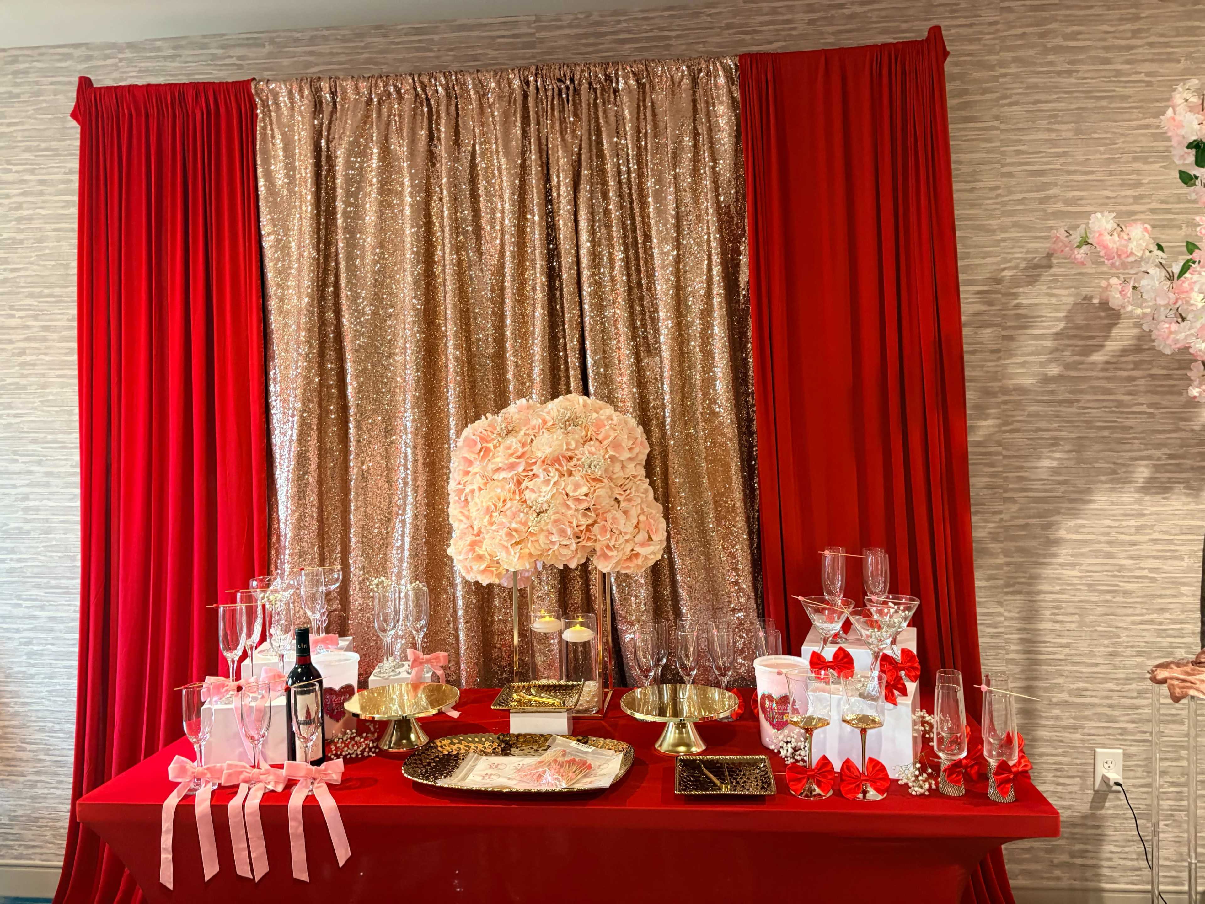 The scene features a decorated table with a red tablecloth, adorned with a large floral centerpiece, various glassware, and sparkling decorations against a shimmering golden backdrop.