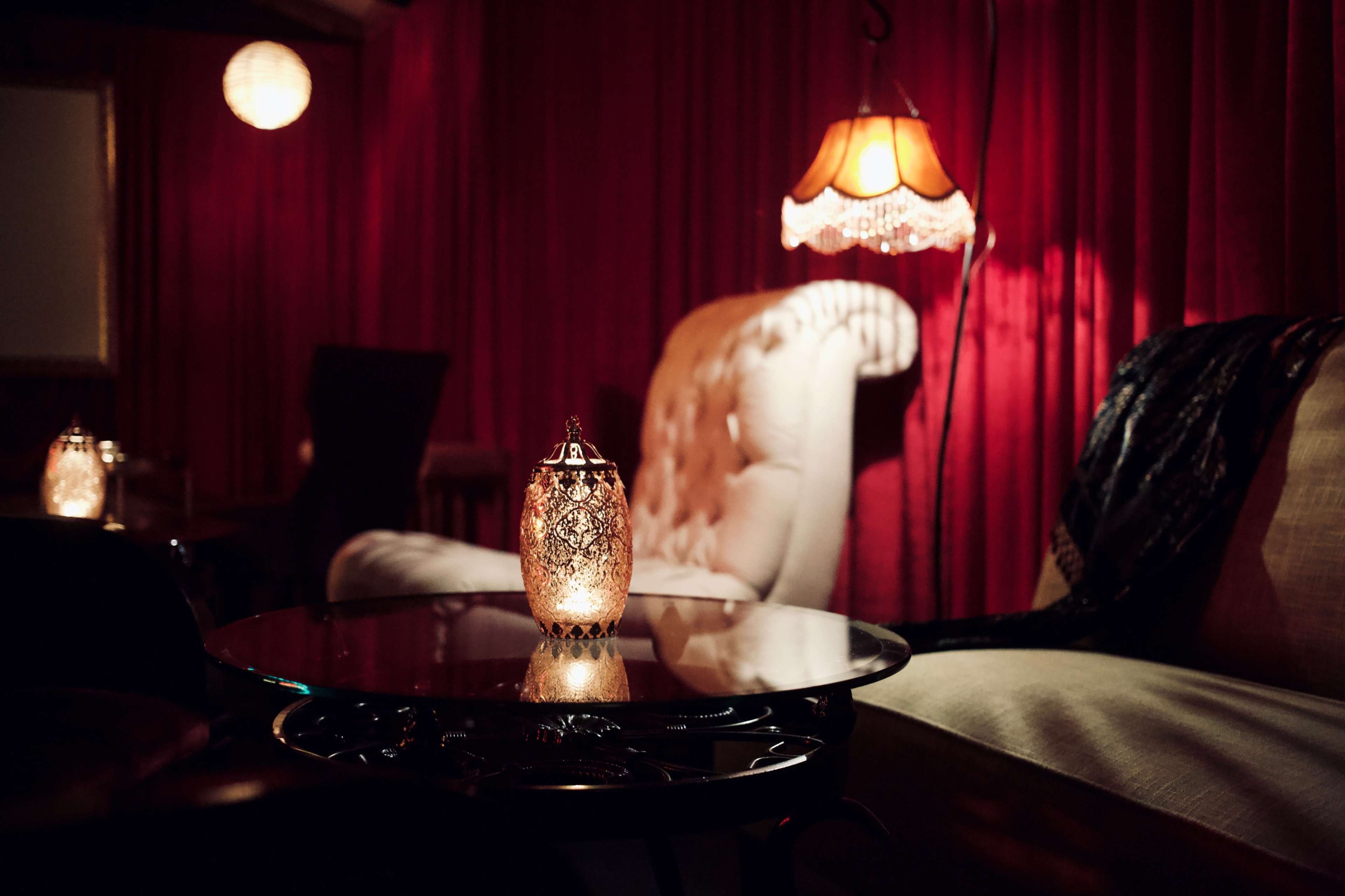 The scene features a dimly lit room with plush seating, a gold-accented lamp, and decorative lanterns on a dark wooden table.