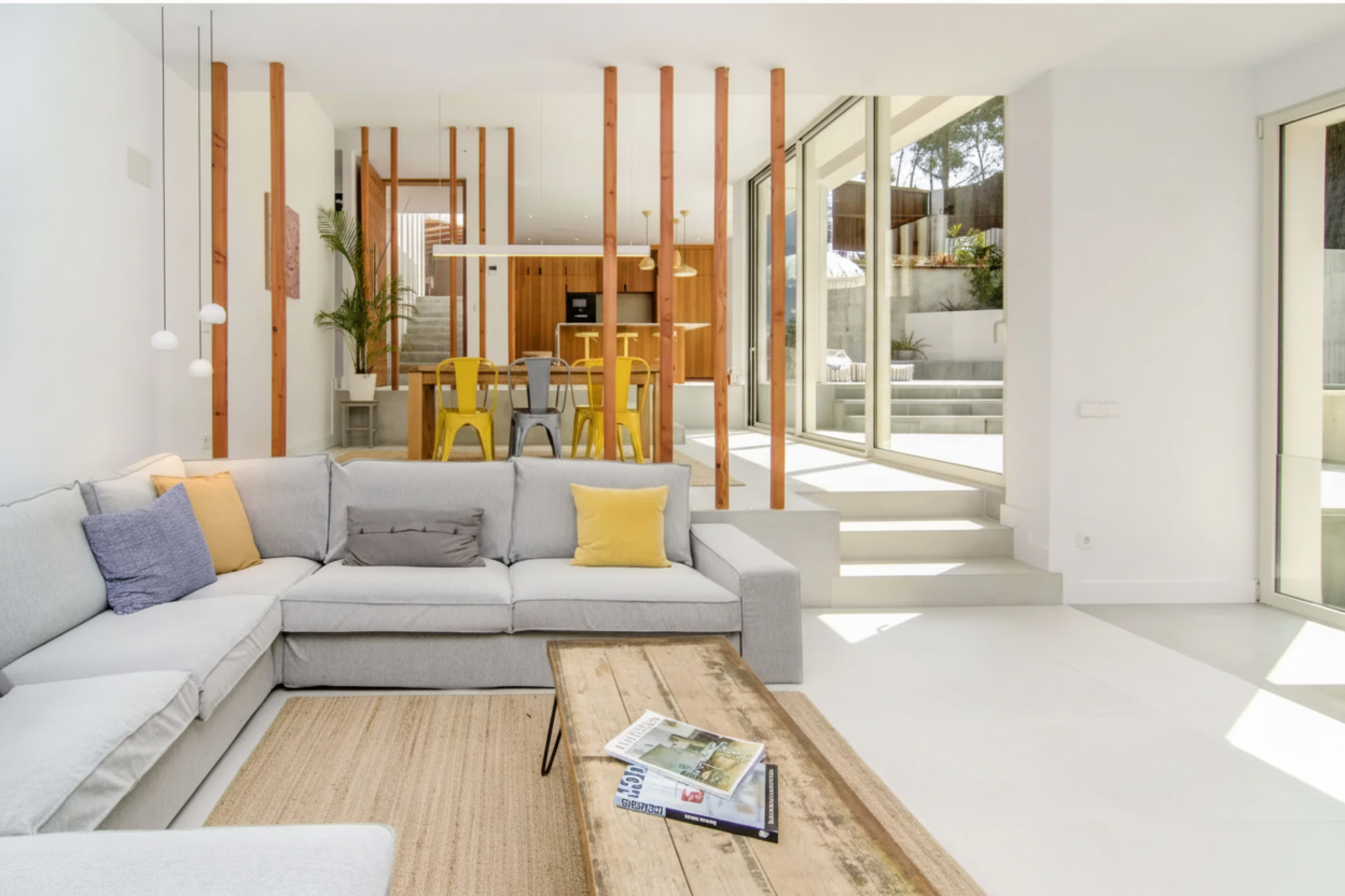 The image shows a modern living room with a gray sectional sofa, a wooden coffee table, and large glass doors opening to an outdoor space.