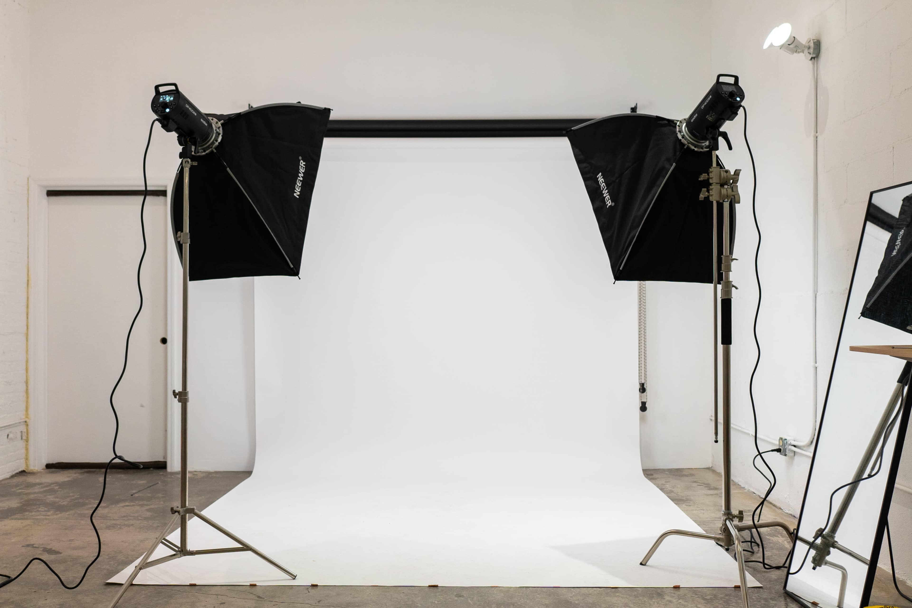 A photography studio setup with two light stands positioned on either side of a blank white backdrop.