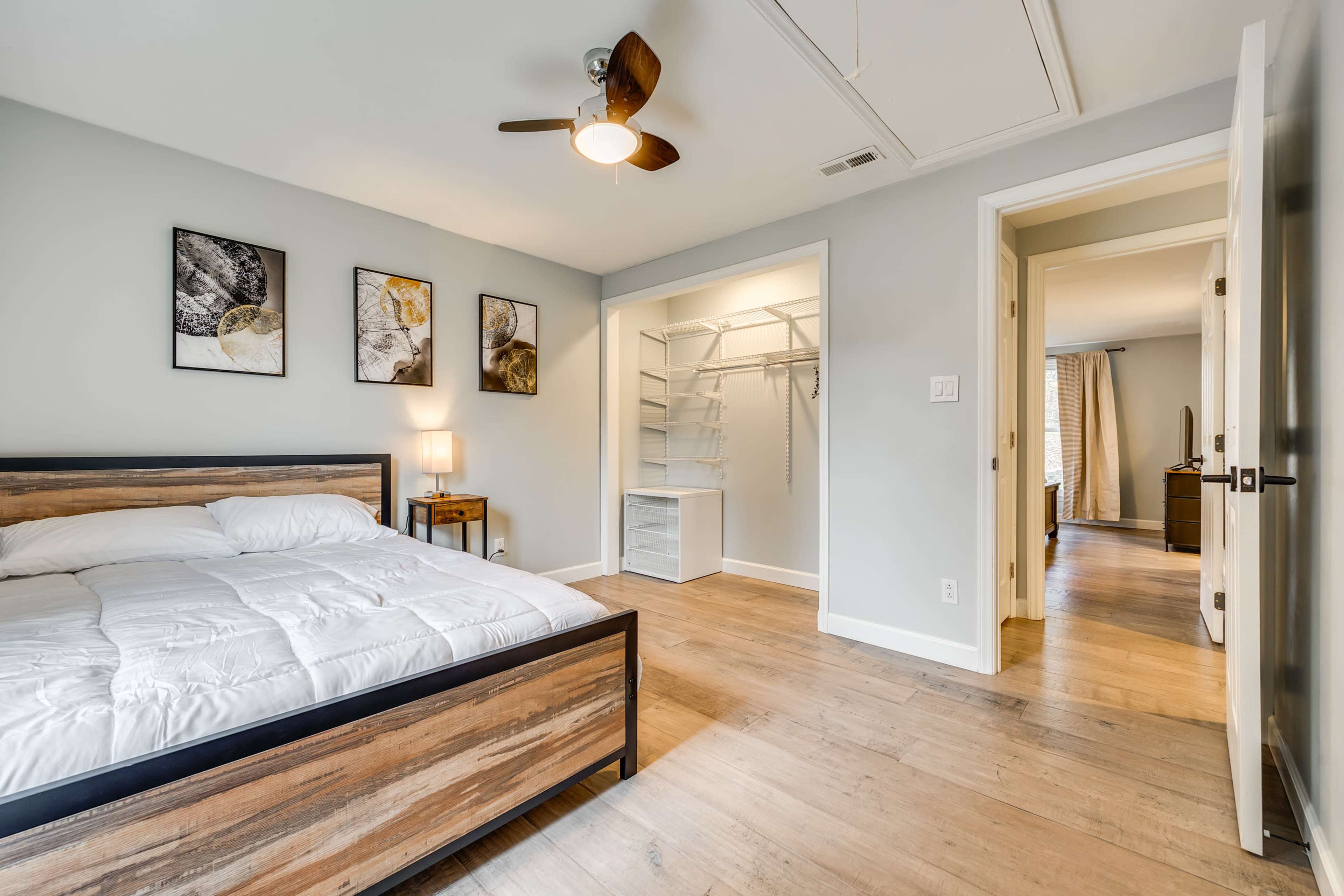 A minimalist bedroom featuring a bed with a wooden frame, two framed artworks on the wall, and a closet area with open shelving.