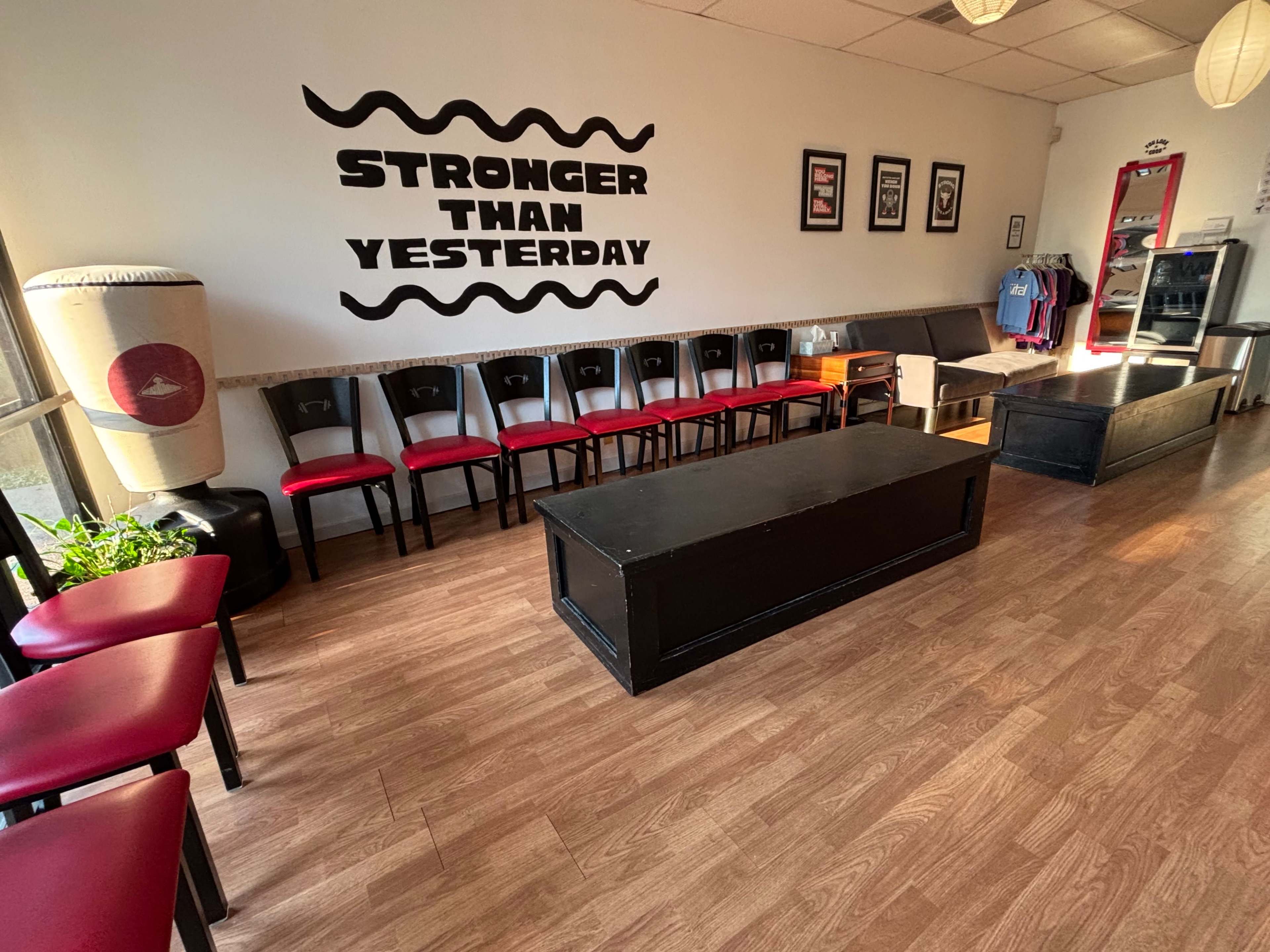 The image shows a neatly arranged indoor space with red and black chairs lining one side, a central black wooden table, and a motivational phrase on the wall.