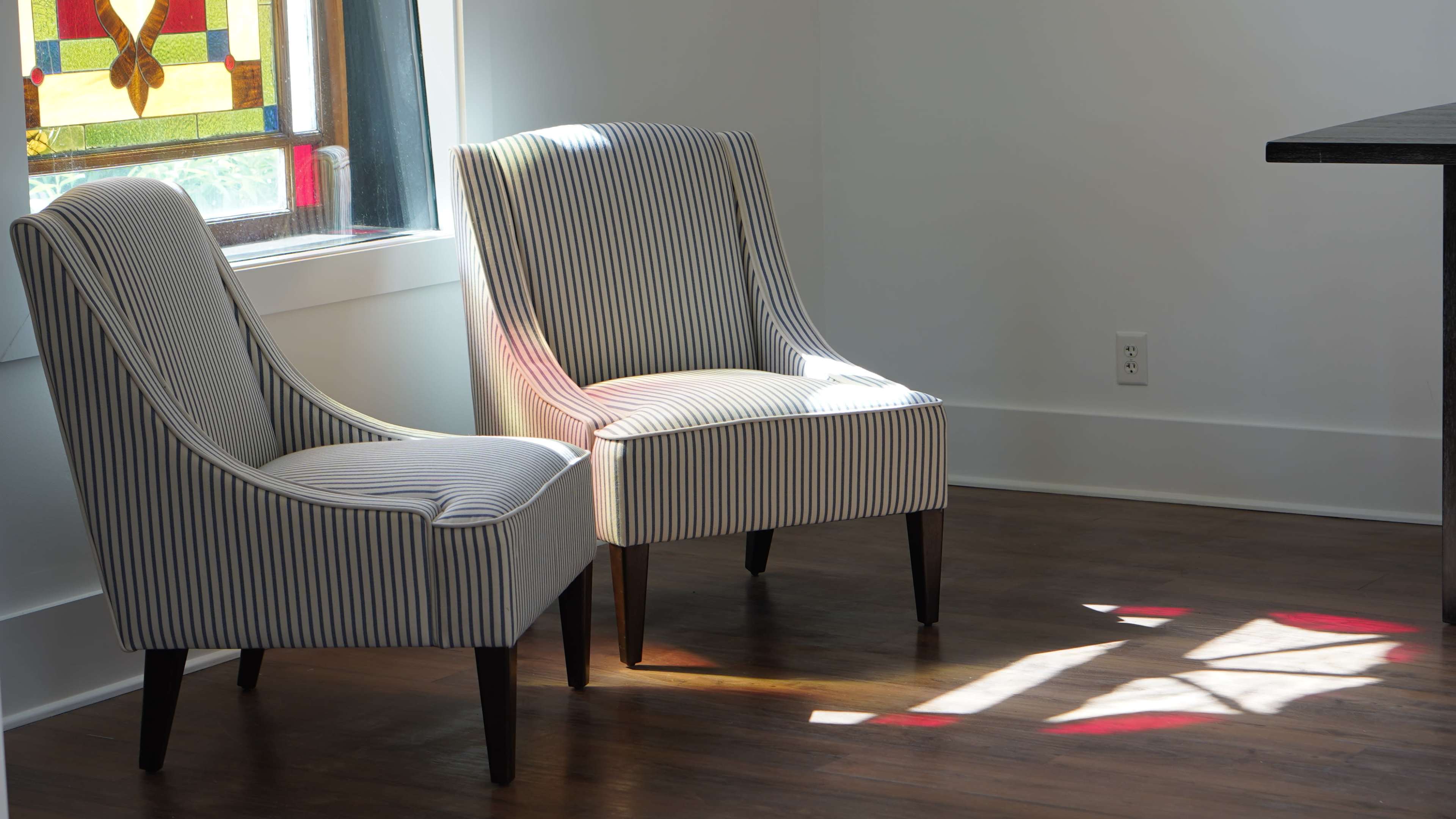 Two striped chairs sit beside a stained glass window, casting colorful light on the wooden floor.