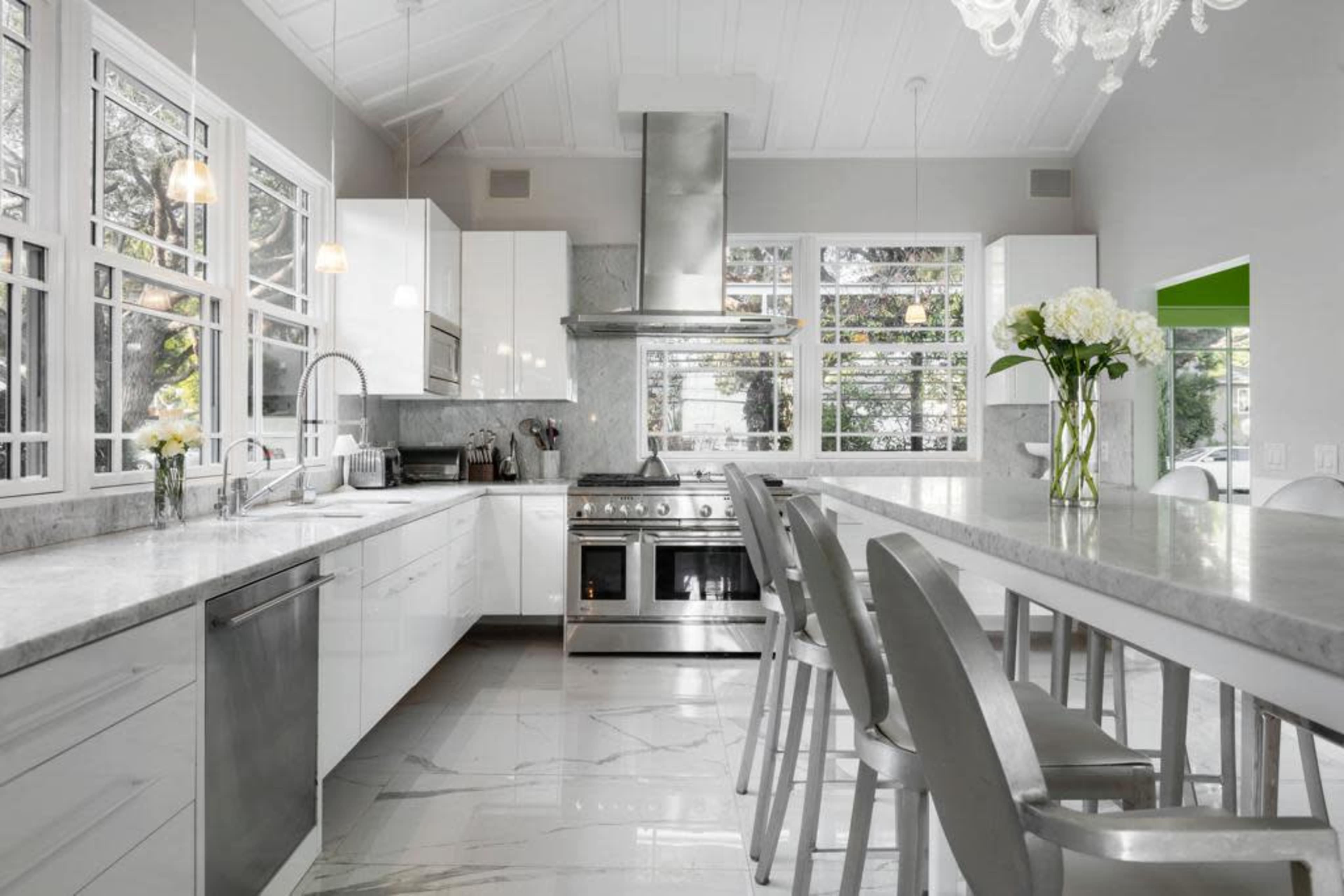 A modern kitchen featuring white cabinetry, a central island with gray countertops, stainless steel appliances, and large windows allowing natural light to enter.
