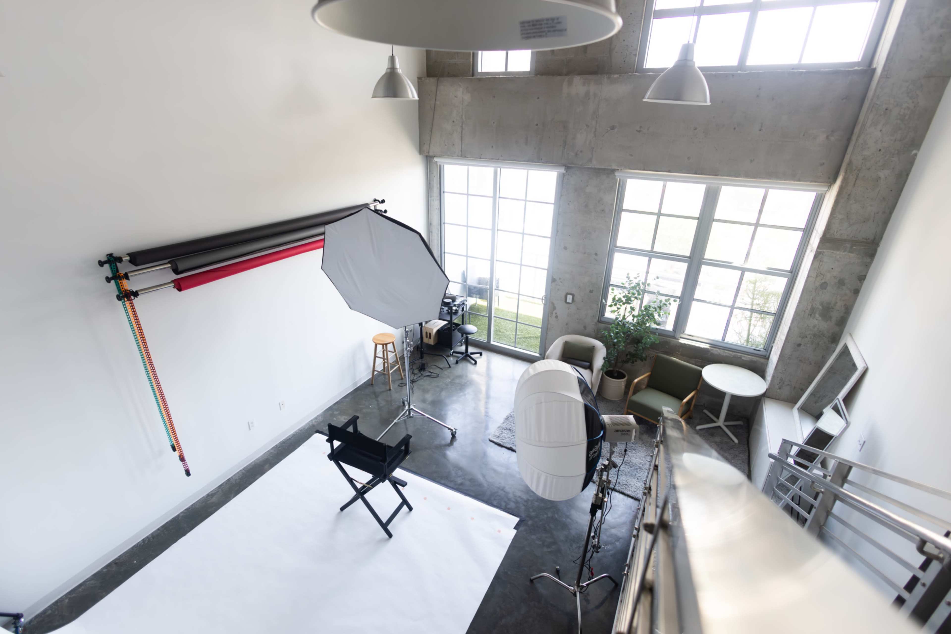 The image shows a well-lit photography studio with large windows, a setup including a backdrop, a director's chair, and several pieces of furniture.