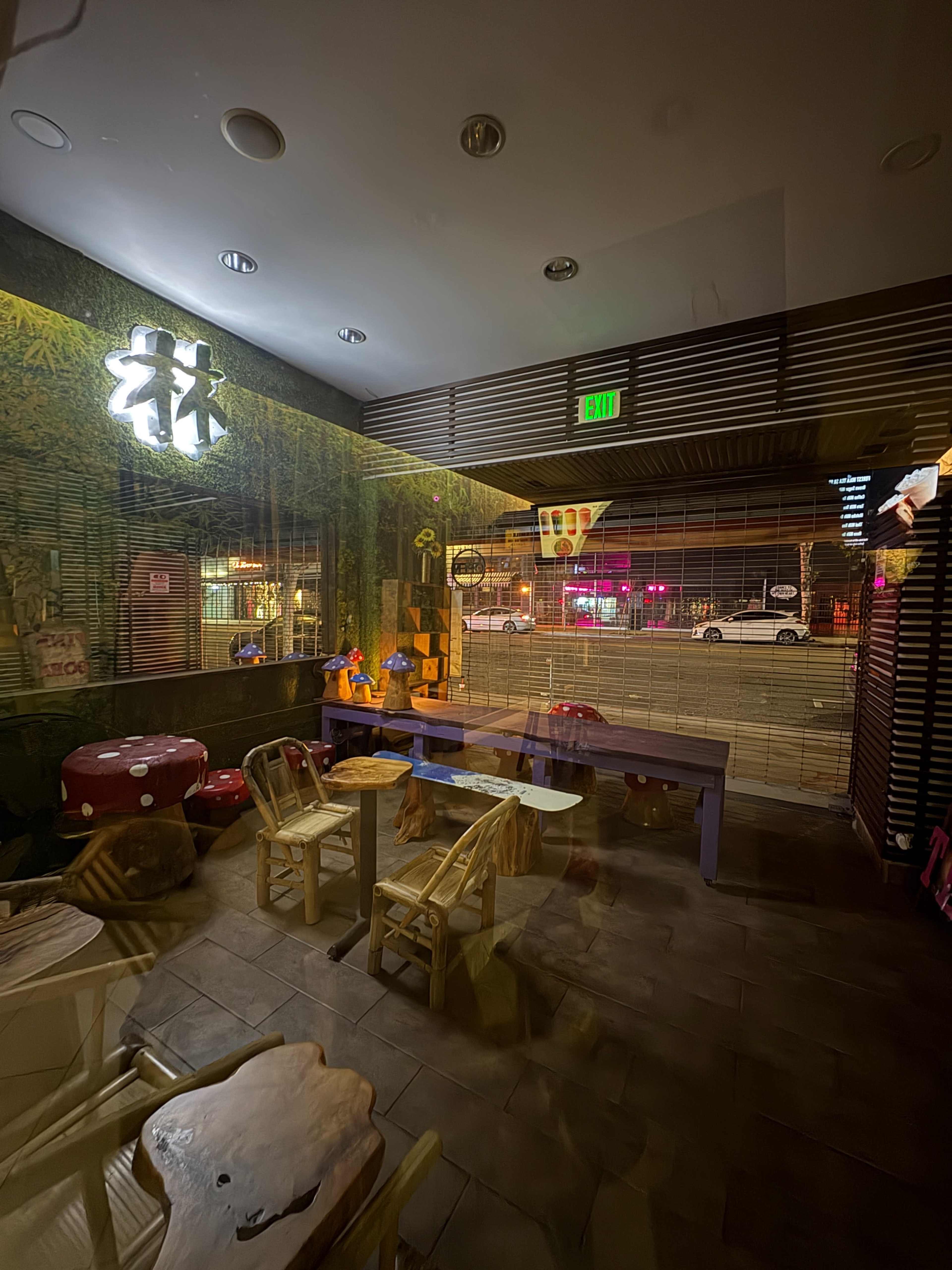 The image shows an interior of a restaurant featuring bamboo decor, wooden furniture, and dim lighting, with a view of a street visible through glass doors.