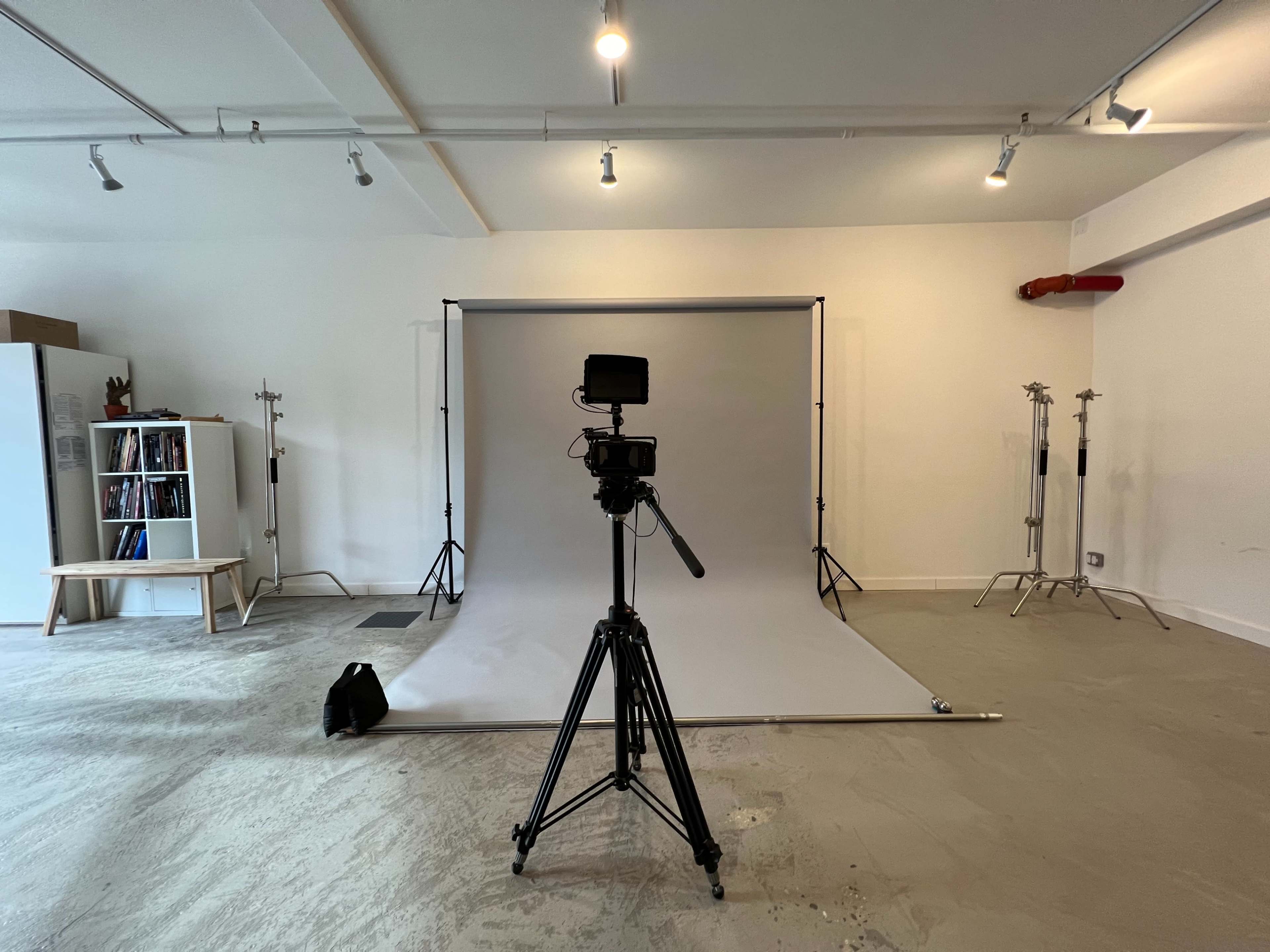 A camera on a tripod faces a gray backdrop in a well-lit studio space.