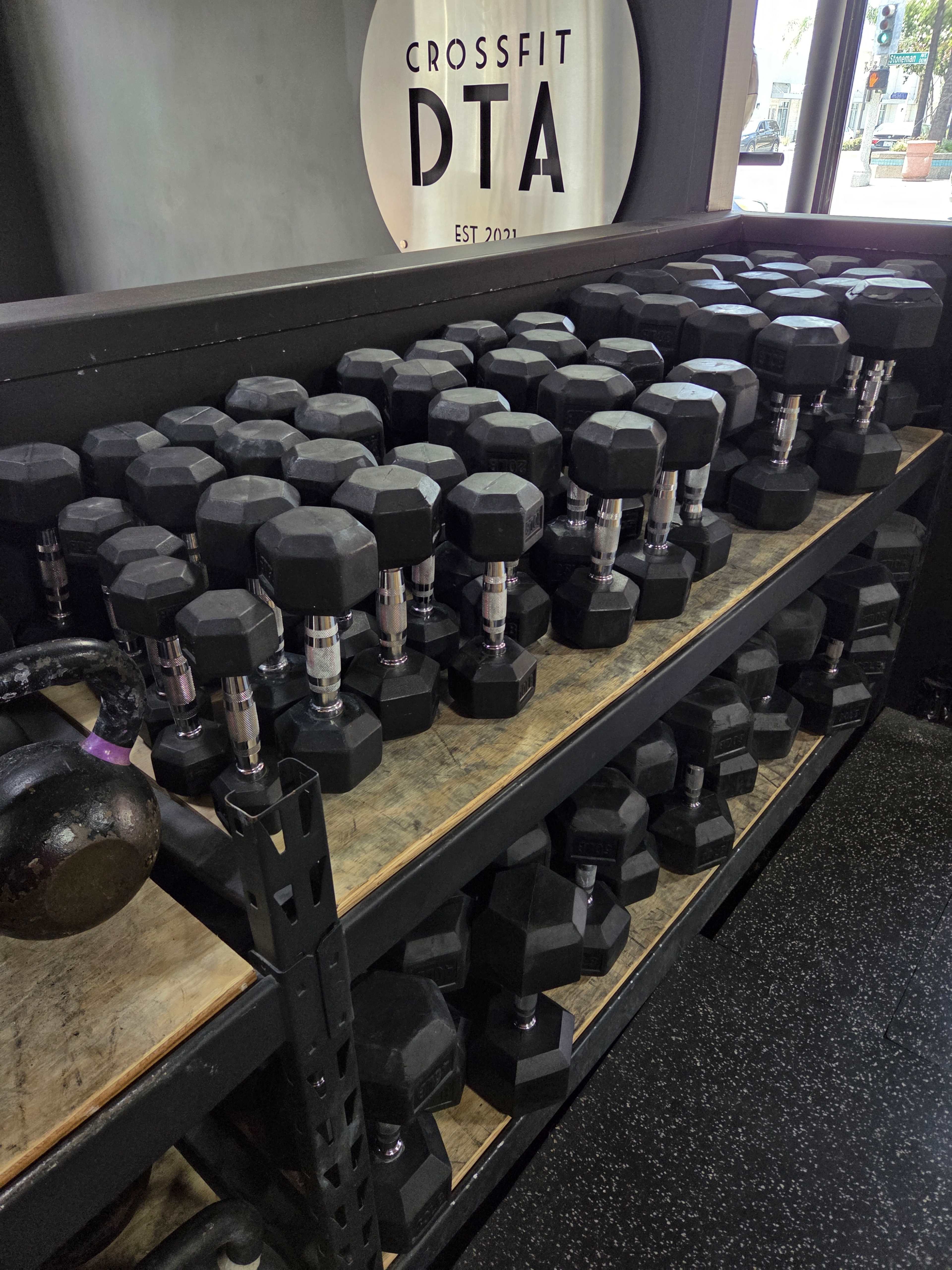 A rack filled with multiple sets of black hexagonal dumbbells is displayed in a fitness gym.