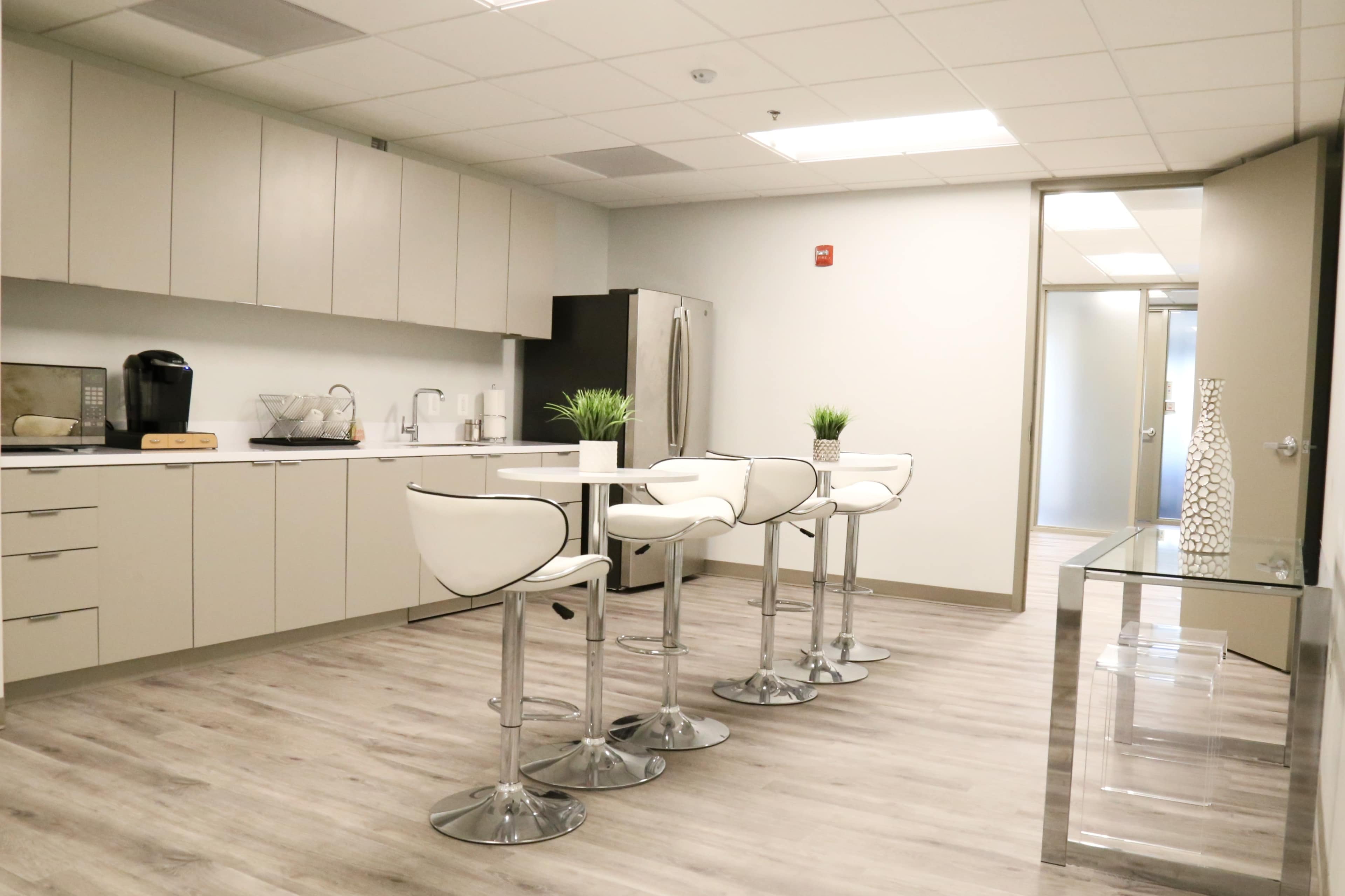 A modern kitchen area featuring sleek cabinets, a table with four high chairs, and stainless steel appliances.