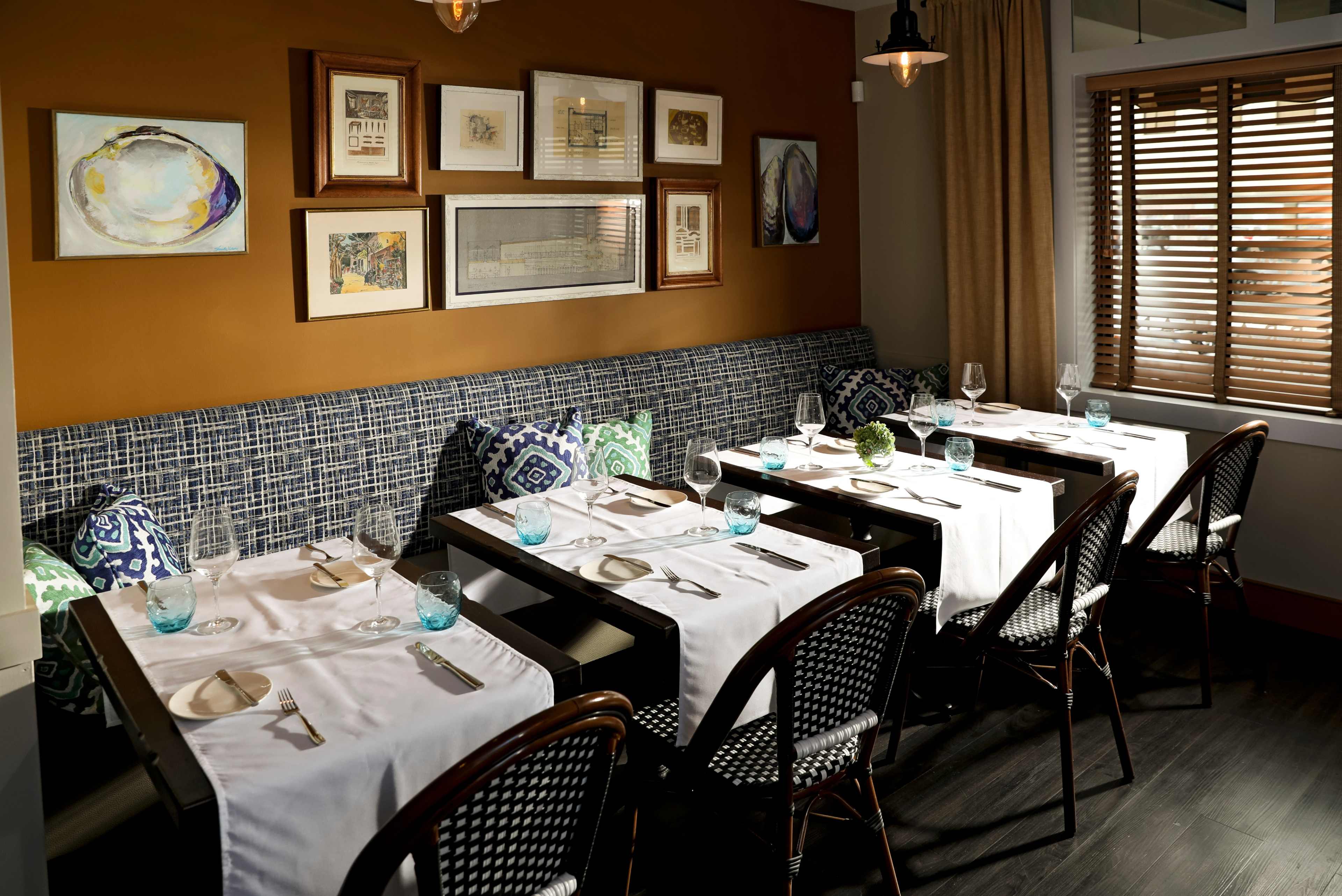 A cozy restaurant setting features neatly arranged tables with white tablecloths, glassware, and decorative wall art.
