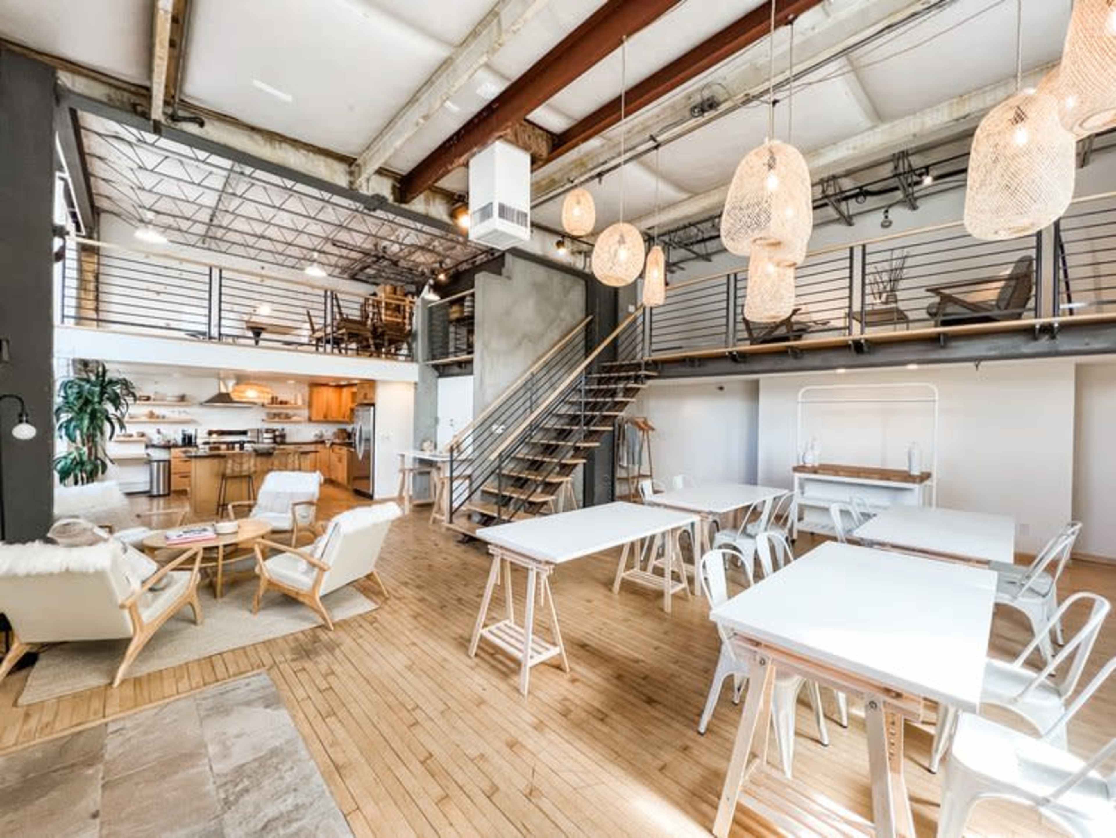 A spacious, modern loft with an open layout featuring wooden floors, a kitchen area, dining tables, and decorative pendant lights.
