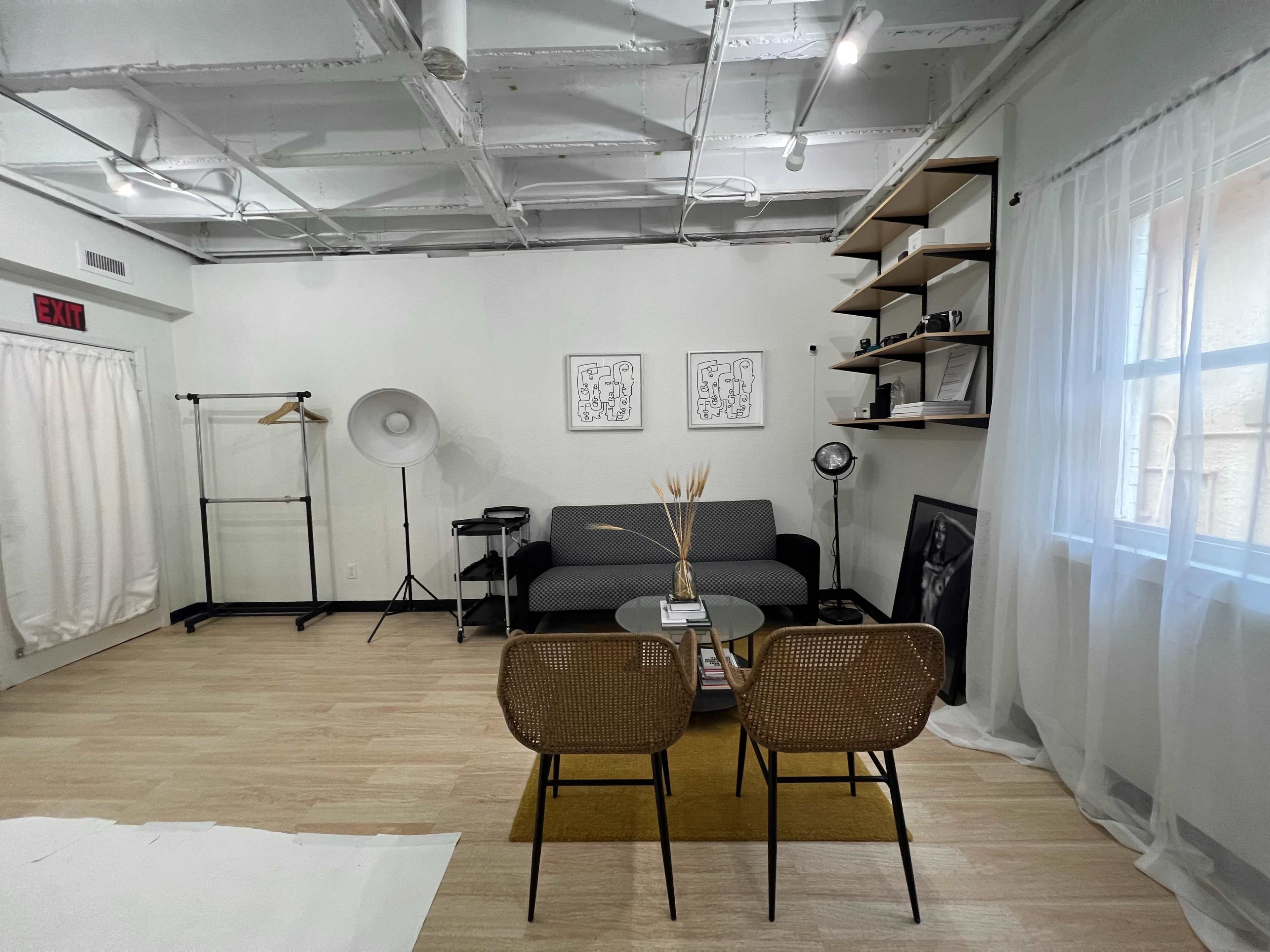 A modern, minimalist room with a gray sofa, two woven chairs, a round coffee table, and decorative elements like a floor lamp and shelving.