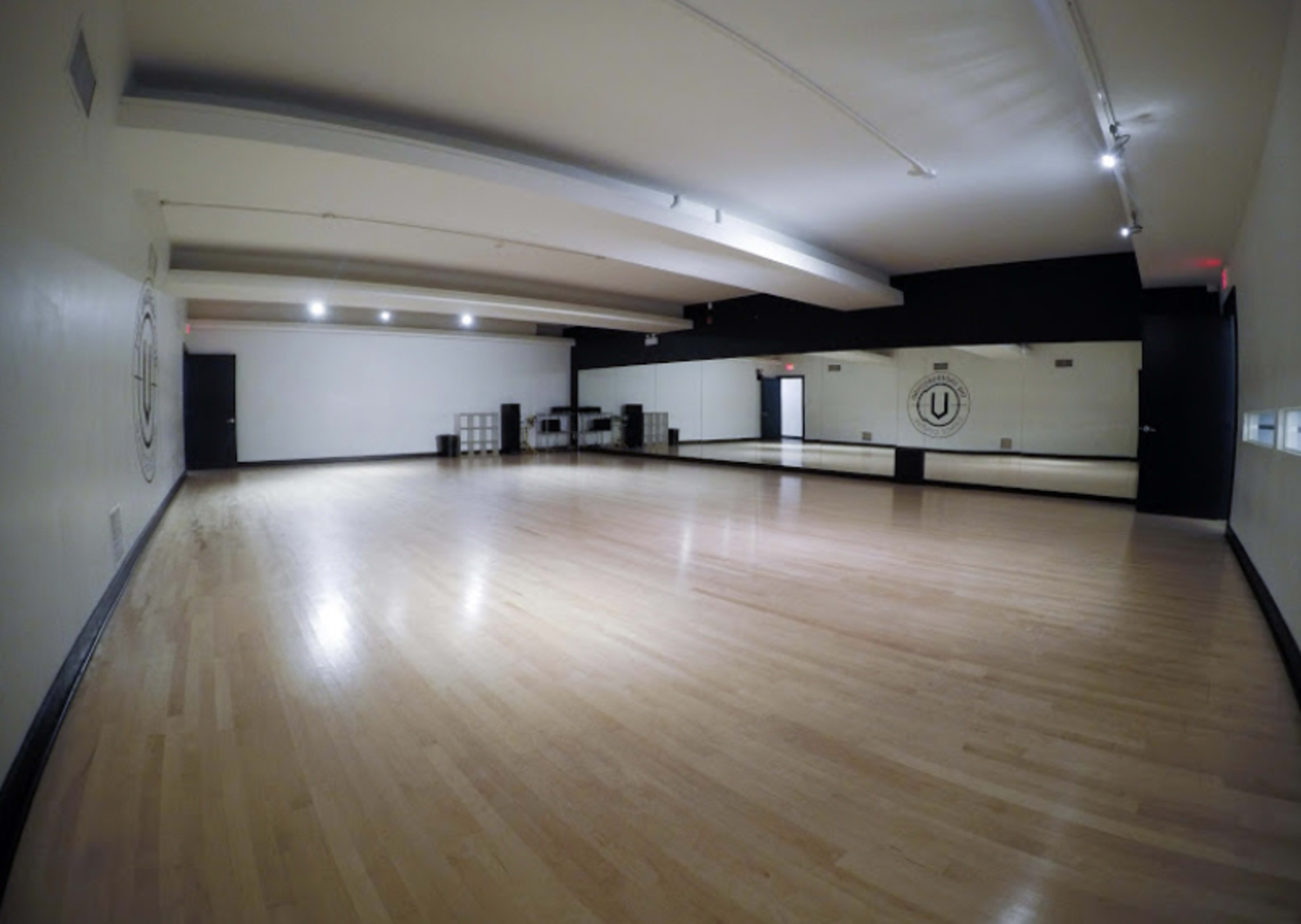 A spacious dance studio with wooden floors, large mirrors on one wall, and minimalistic decor.