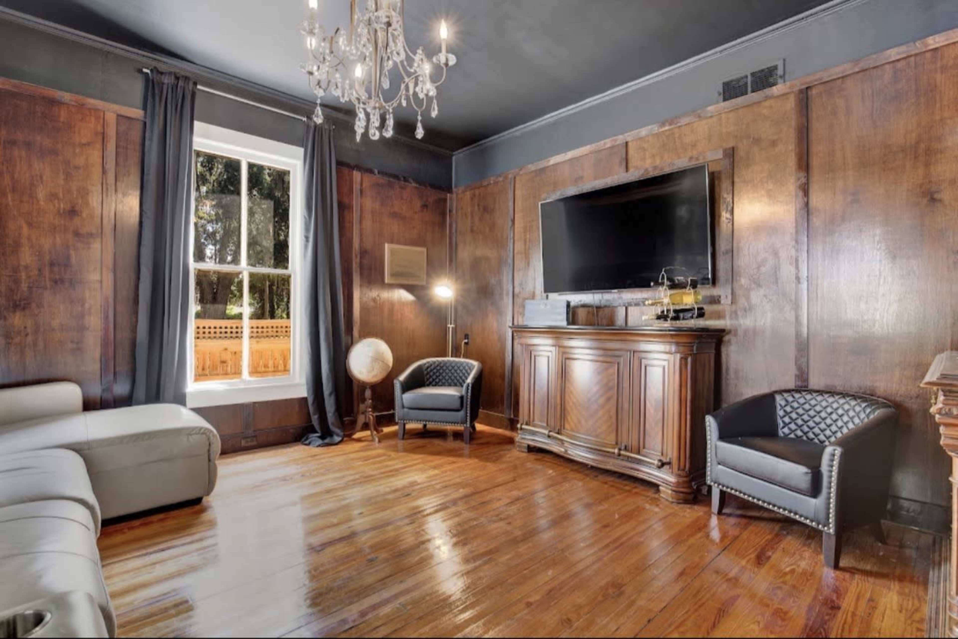 The room features dark wood paneling, a large flat-screen TV mounted on a cabinet, and two stylish chairs alongside a globe.