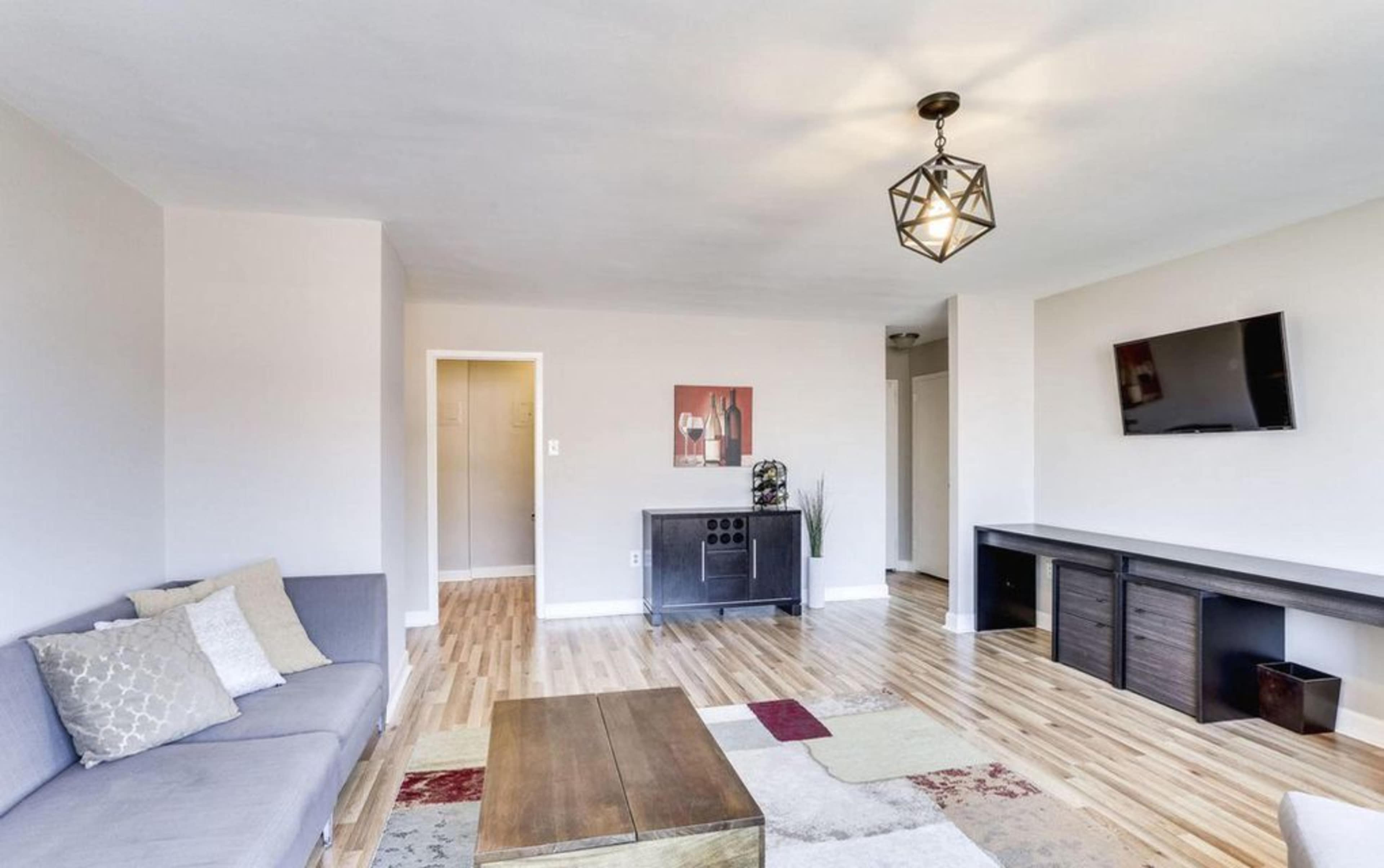 A bright living room featuring a gray couch, a wooden coffee table, and a wall-mounted television.