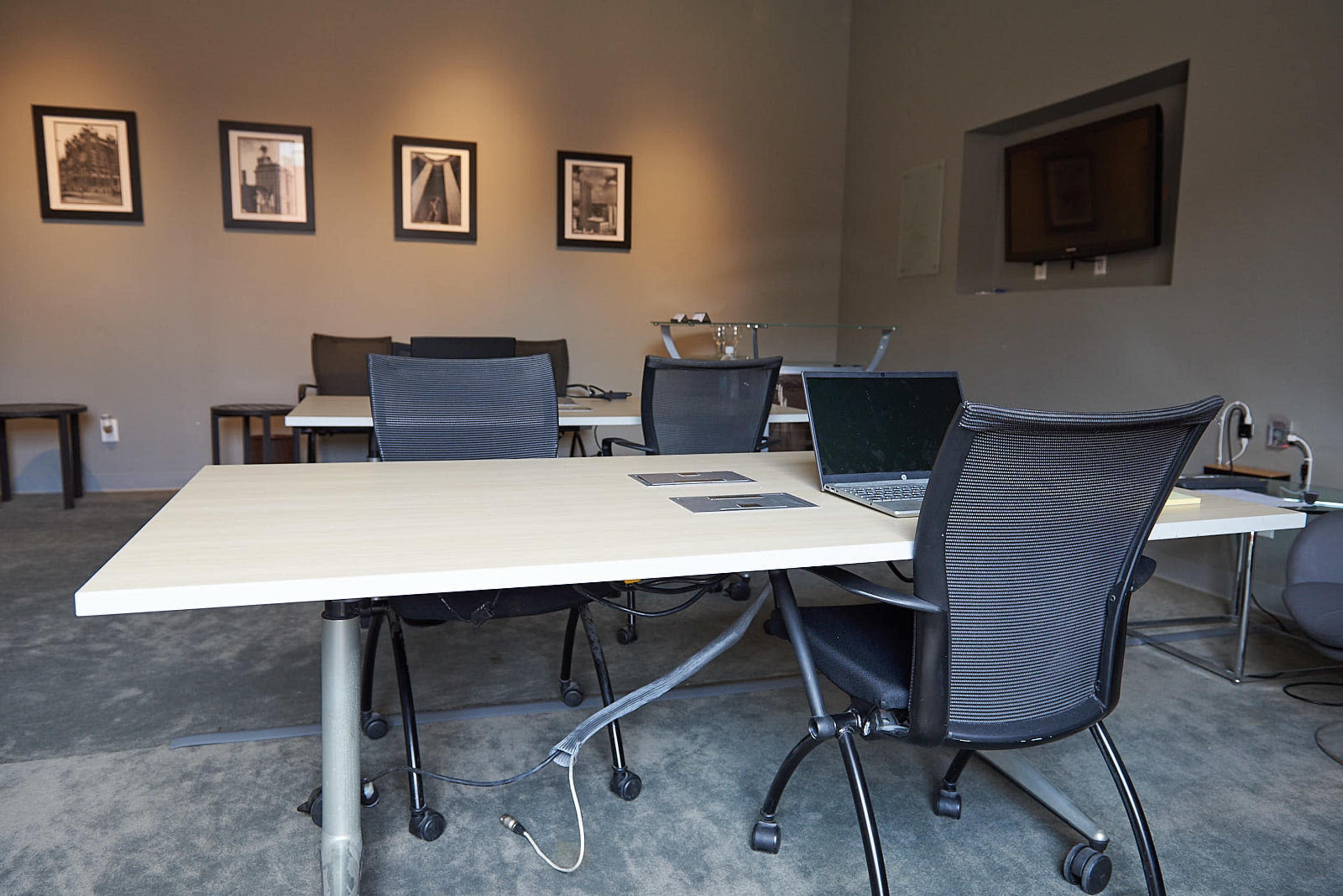 A modern office space with several black chairs and tables arranged around a central area, featuring a laptop on one of the tables and framed photographs on the walls.