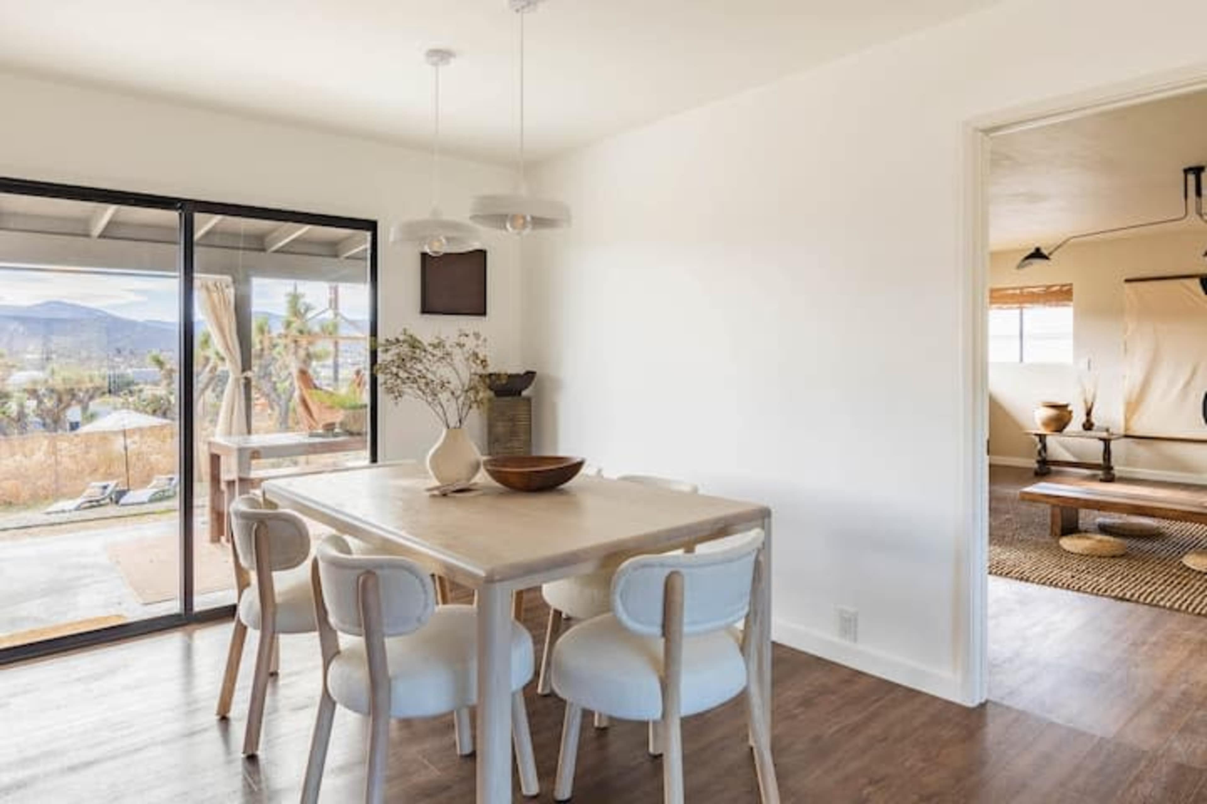 A light-filled dining area features a wooden table surrounded by white chairs, with large sliding doors leading to an outdoor space.