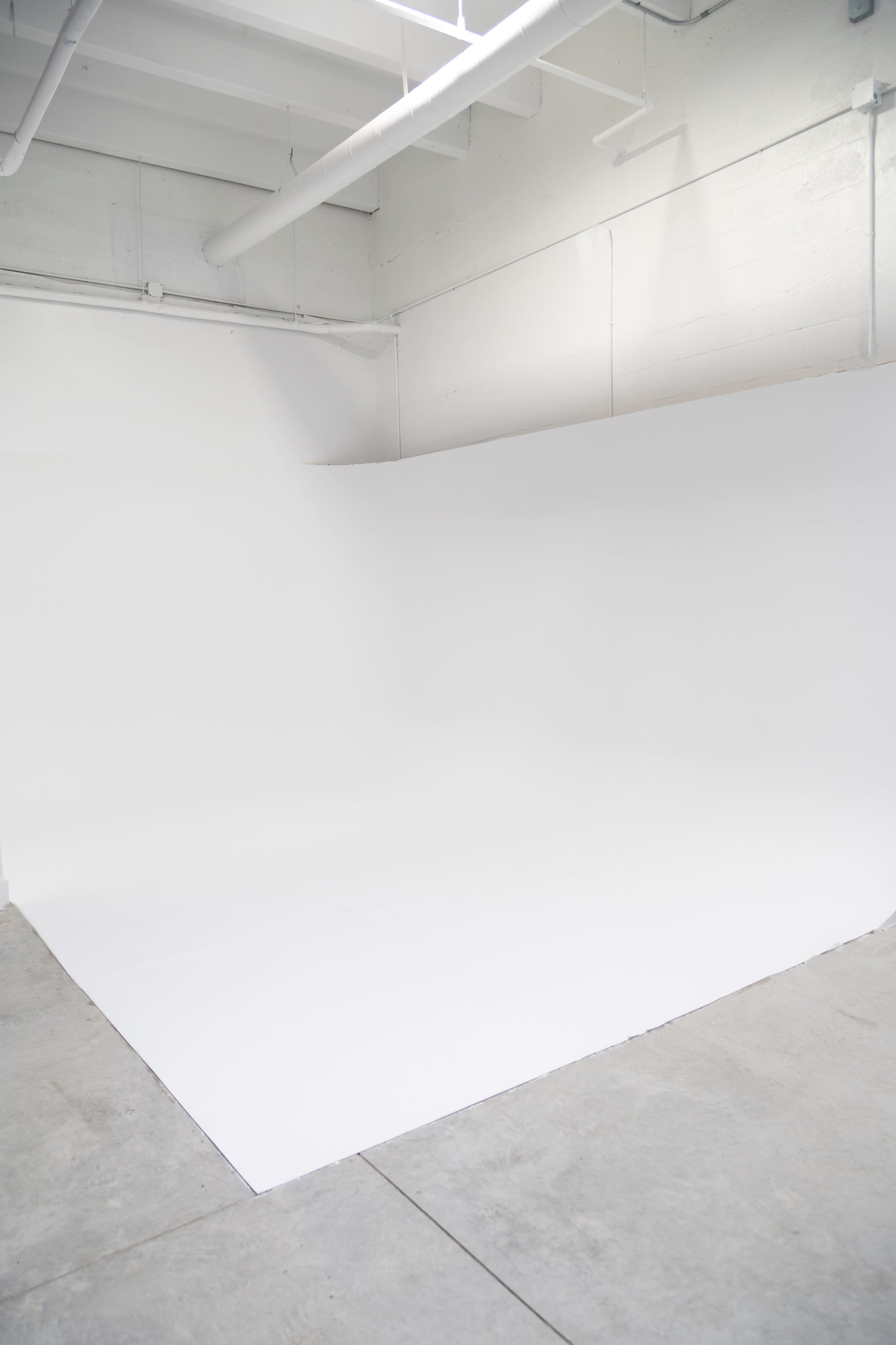 A minimalistic studio space with a seamless white backdrop and concrete flooring.