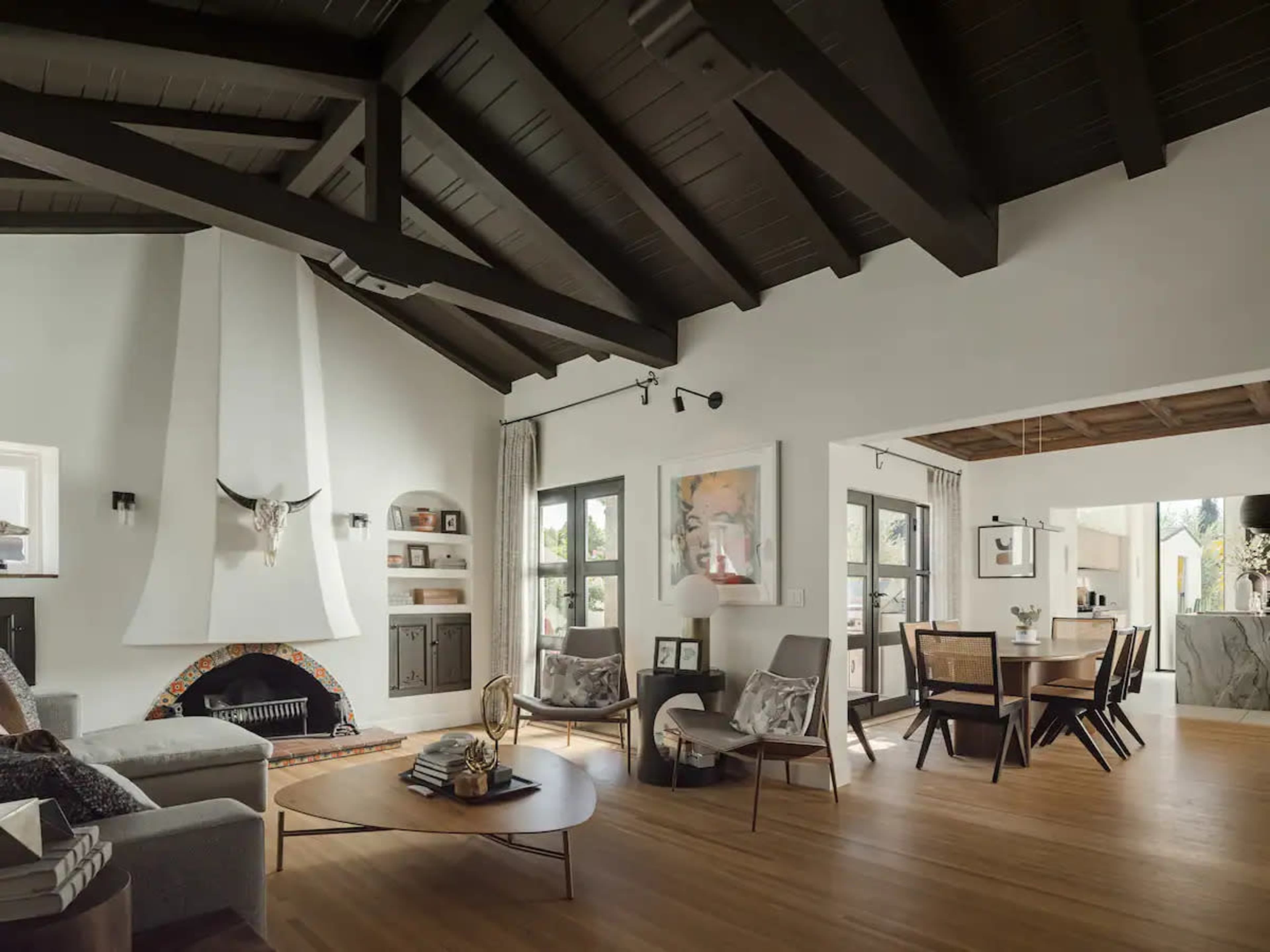 A spacious living room features high wooden ceilings, a modern fireplace with a decorative element, and a connected dining area with a large table.