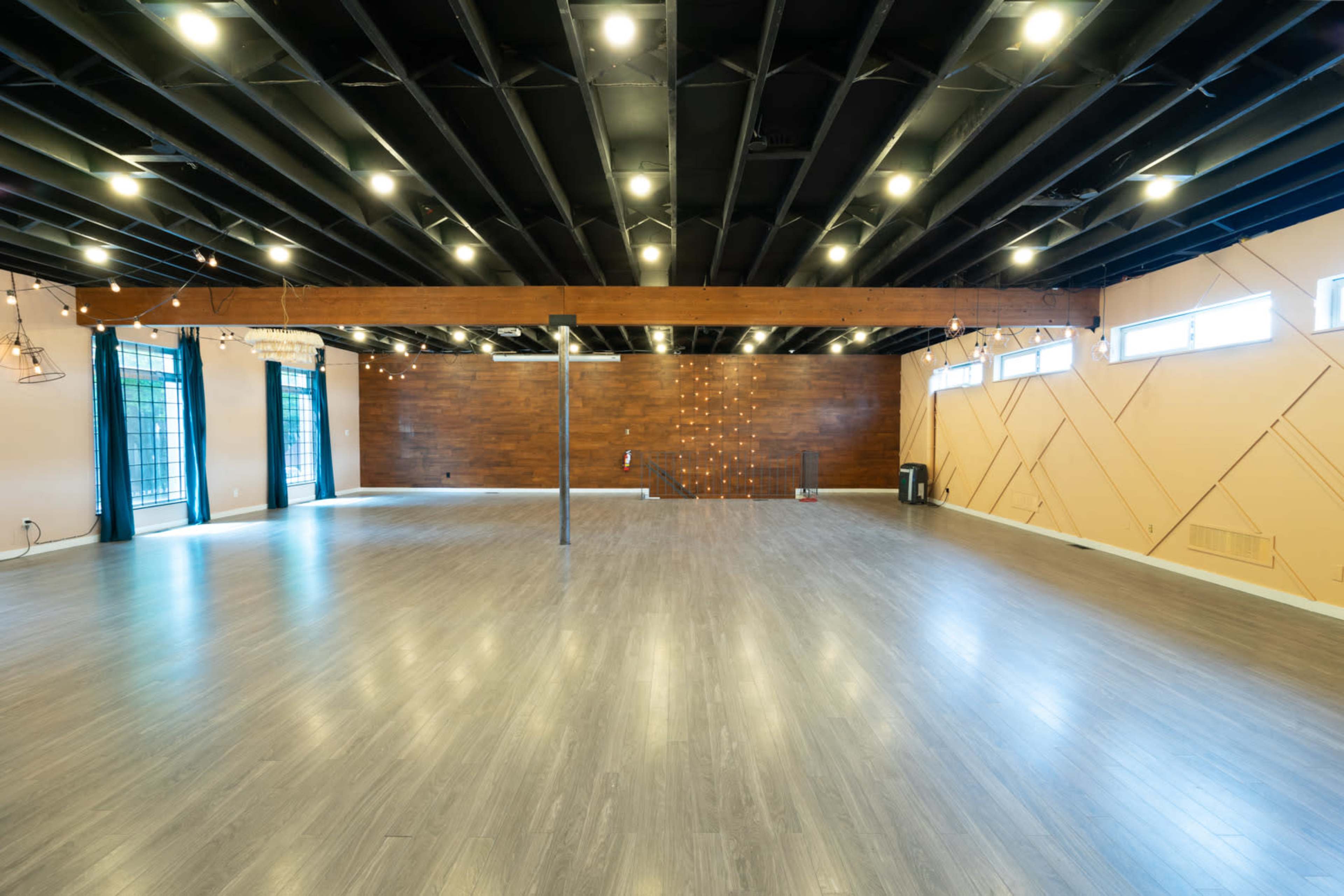 A spacious, empty room with wooden accents, a polished floor, and a black ceiling illuminated by overhead lights.