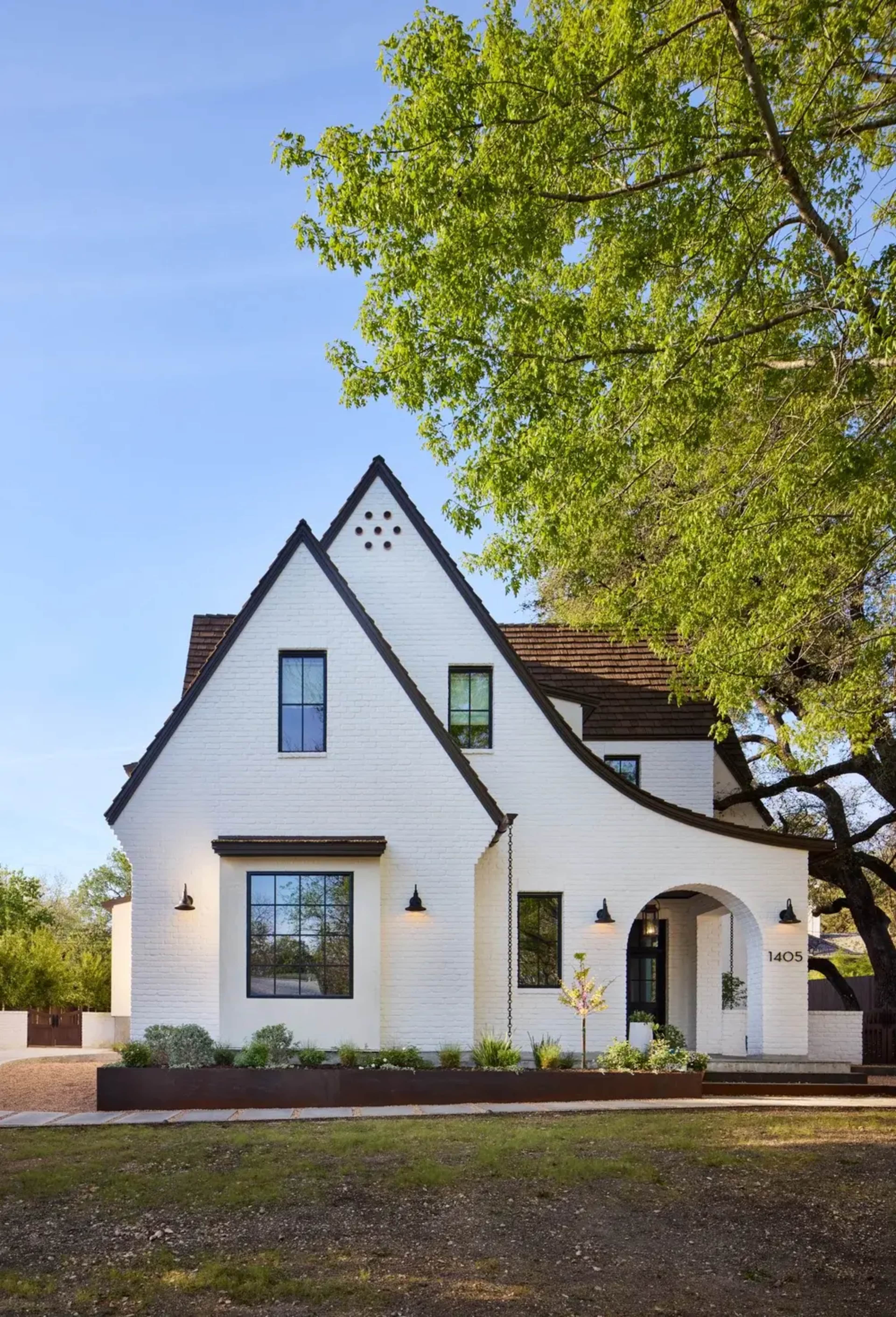 The image features a two-story white house with a distinctive gable roof and a landscaped front yard.