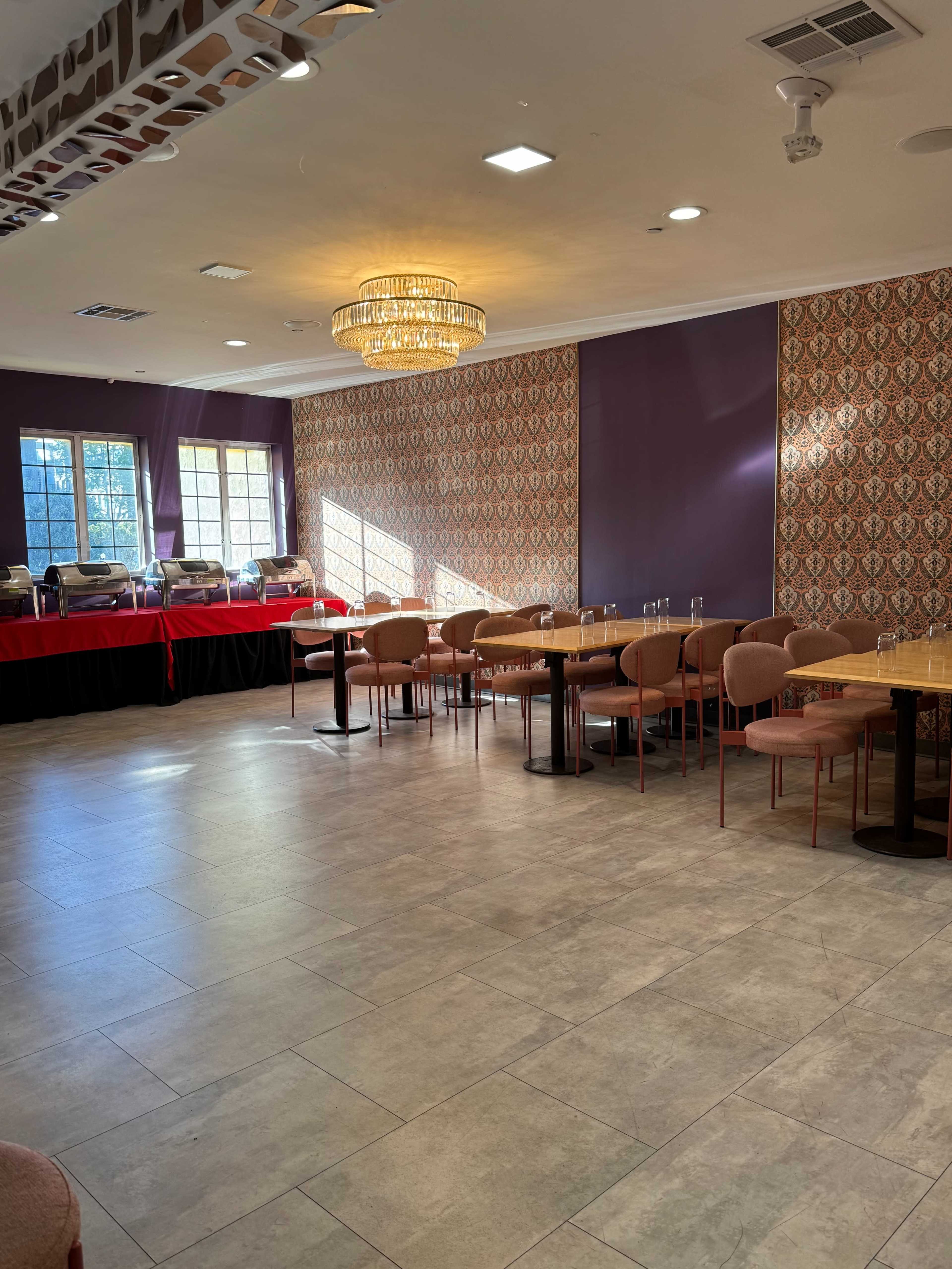 The image shows a well-lit restaurant interior with several tables and chairs arranged, and decorative wallpaper in a patterned design.