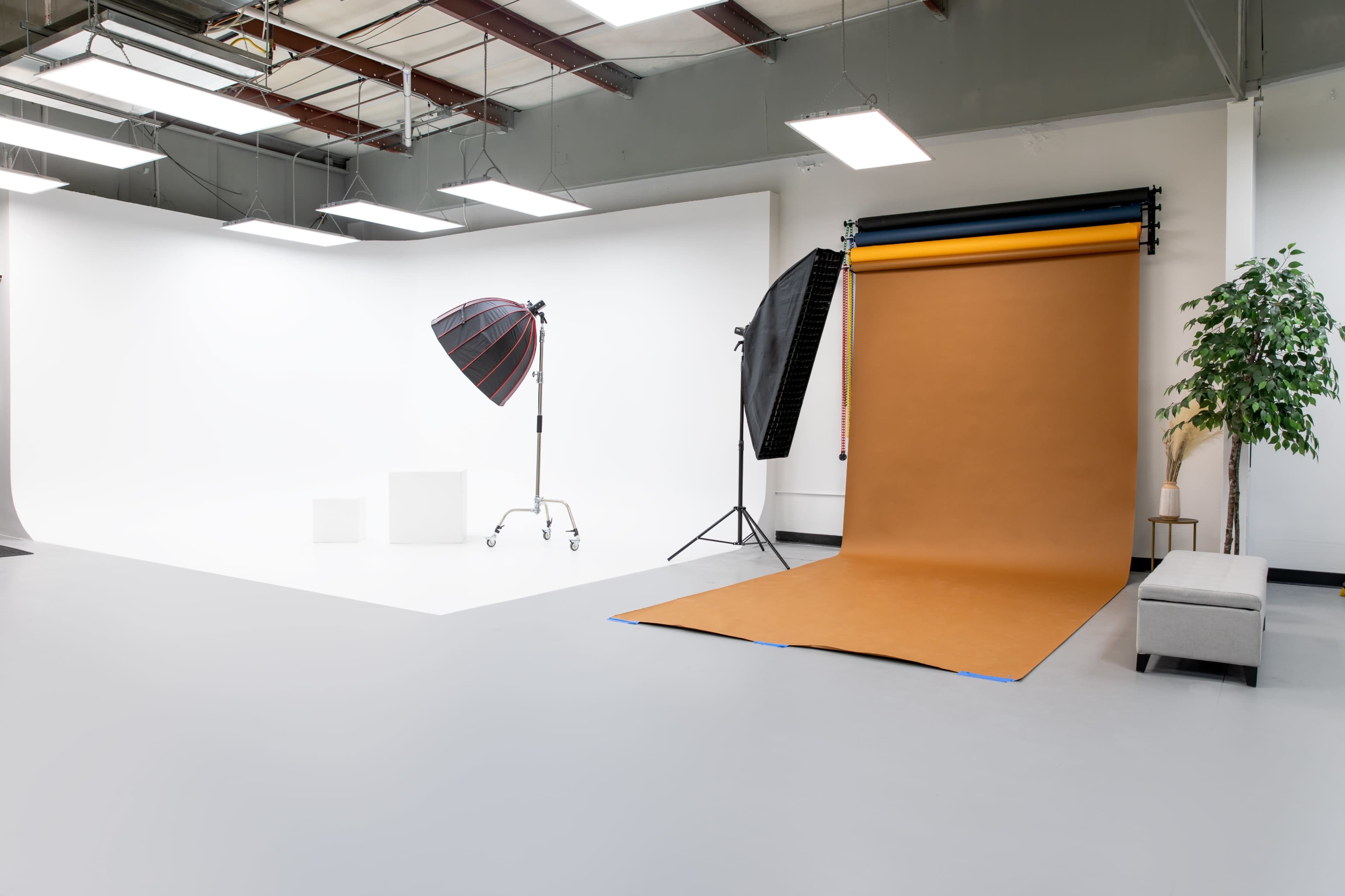 A photography studio featuring a brown backdrop, lighting equipment, and a gray bench against a white wall.