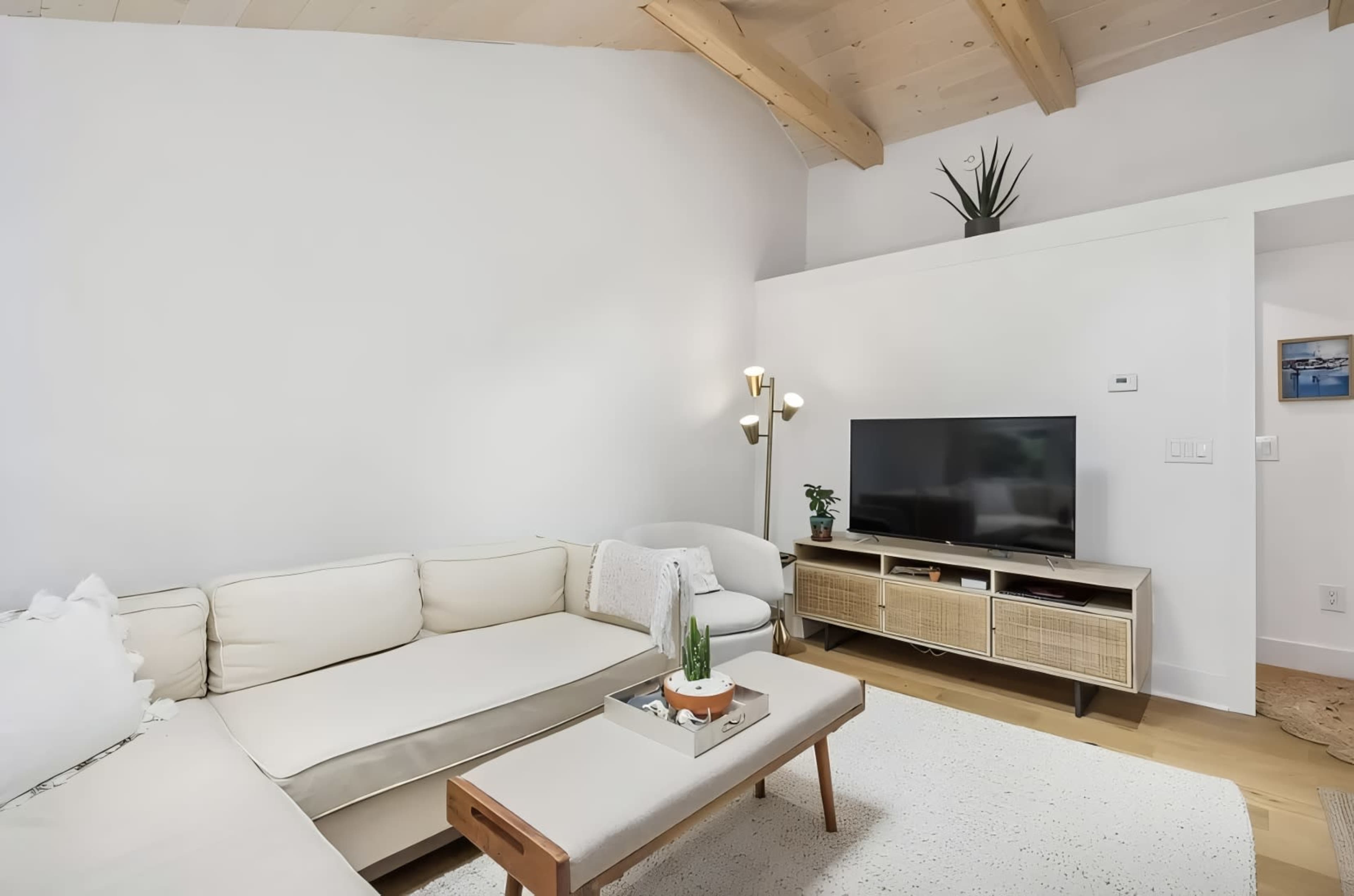 The living room features a sectional sofa, a television on a stand, and a light-colored rug under a vaulted ceiling.