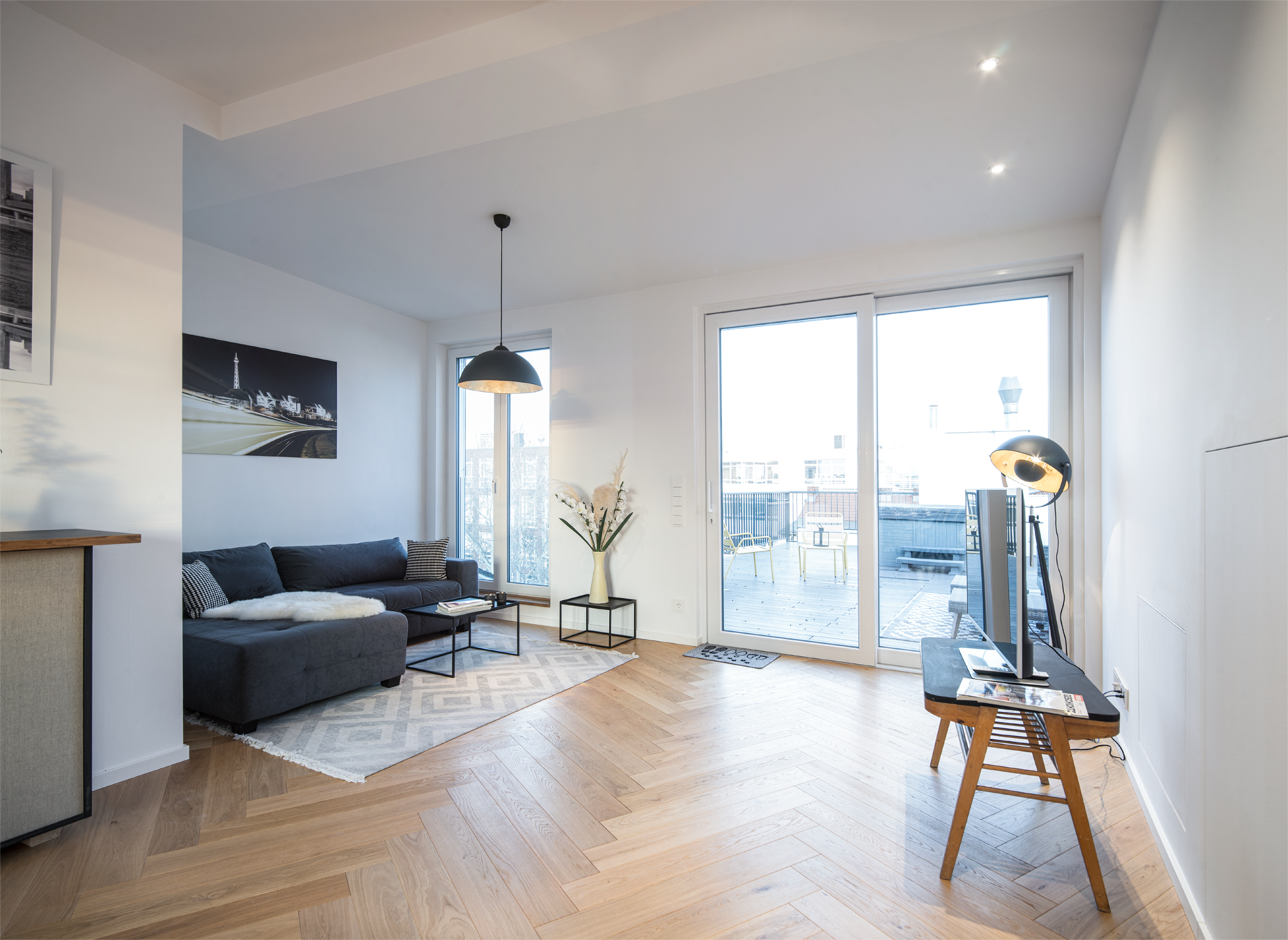 A modern living room with a gray sofa, a coffee table, large windows revealing an outdoor area, and minimalist decor.