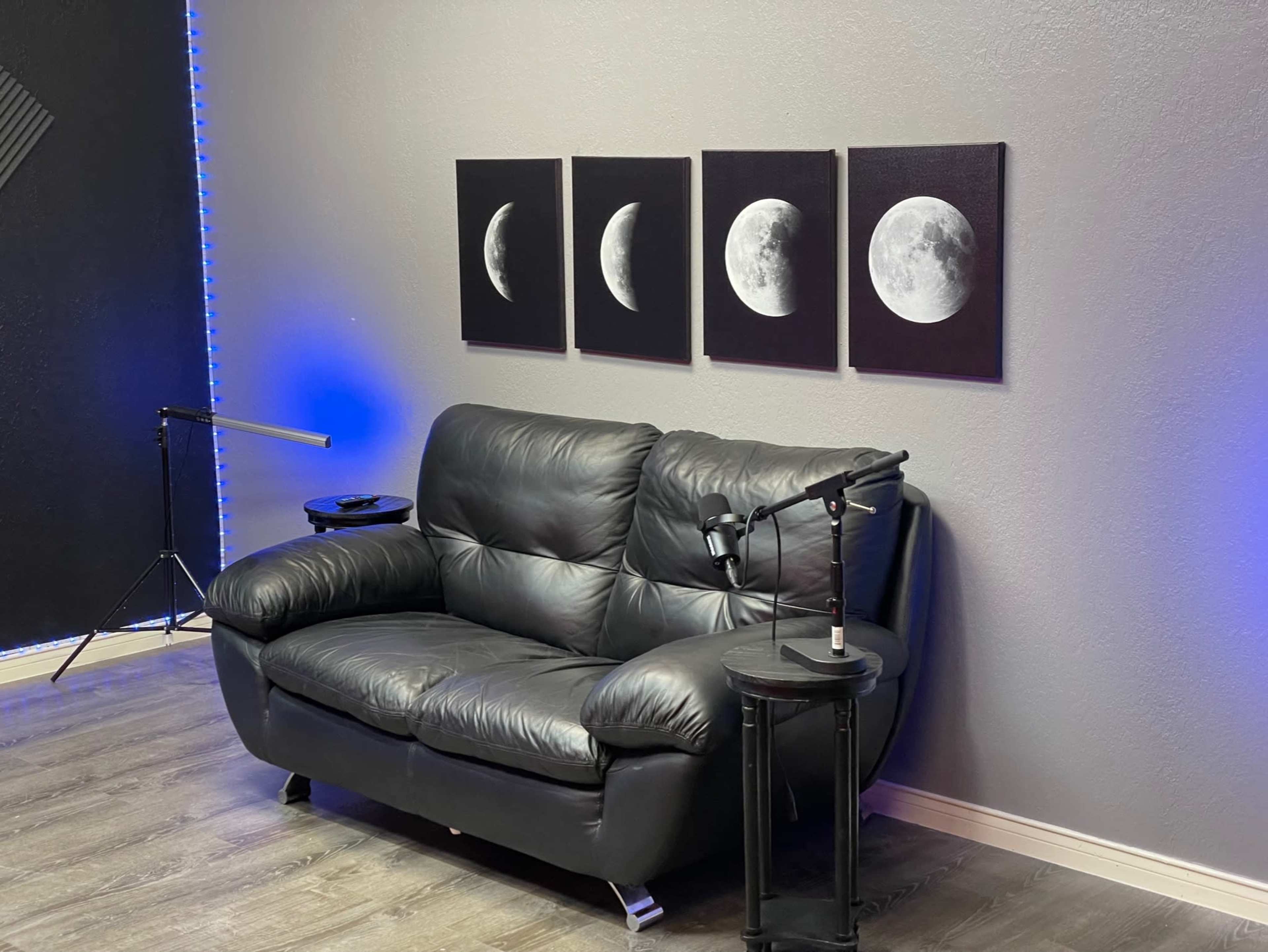 The image shows a black leather couch situated against a gray wall, accompanied by four moon phase canvas prints and a small side table with a microphone.