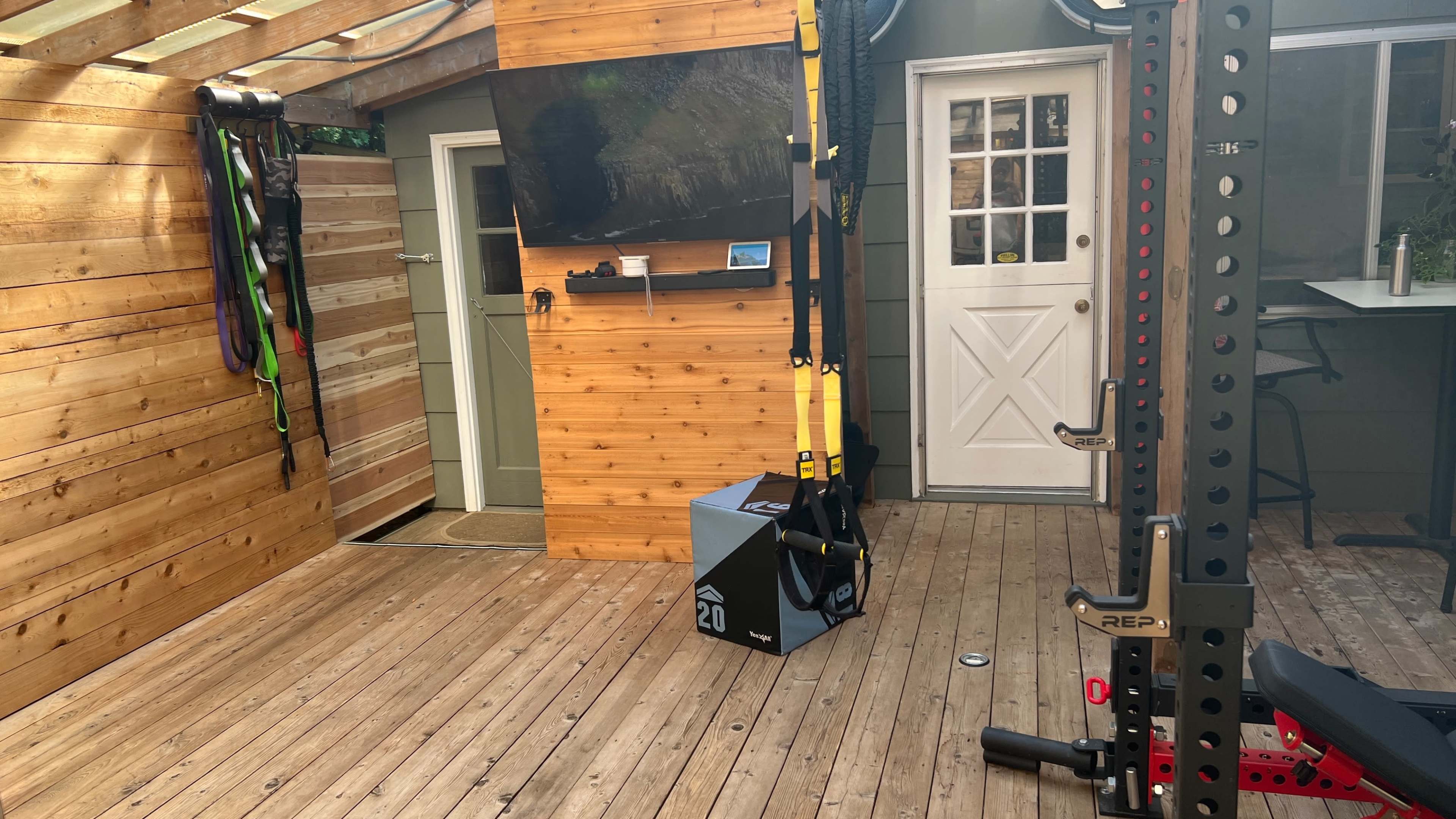 A well-equipped home gym featuring a wooden interior, a wall-mounted television, exercise bands, and a weight rack.