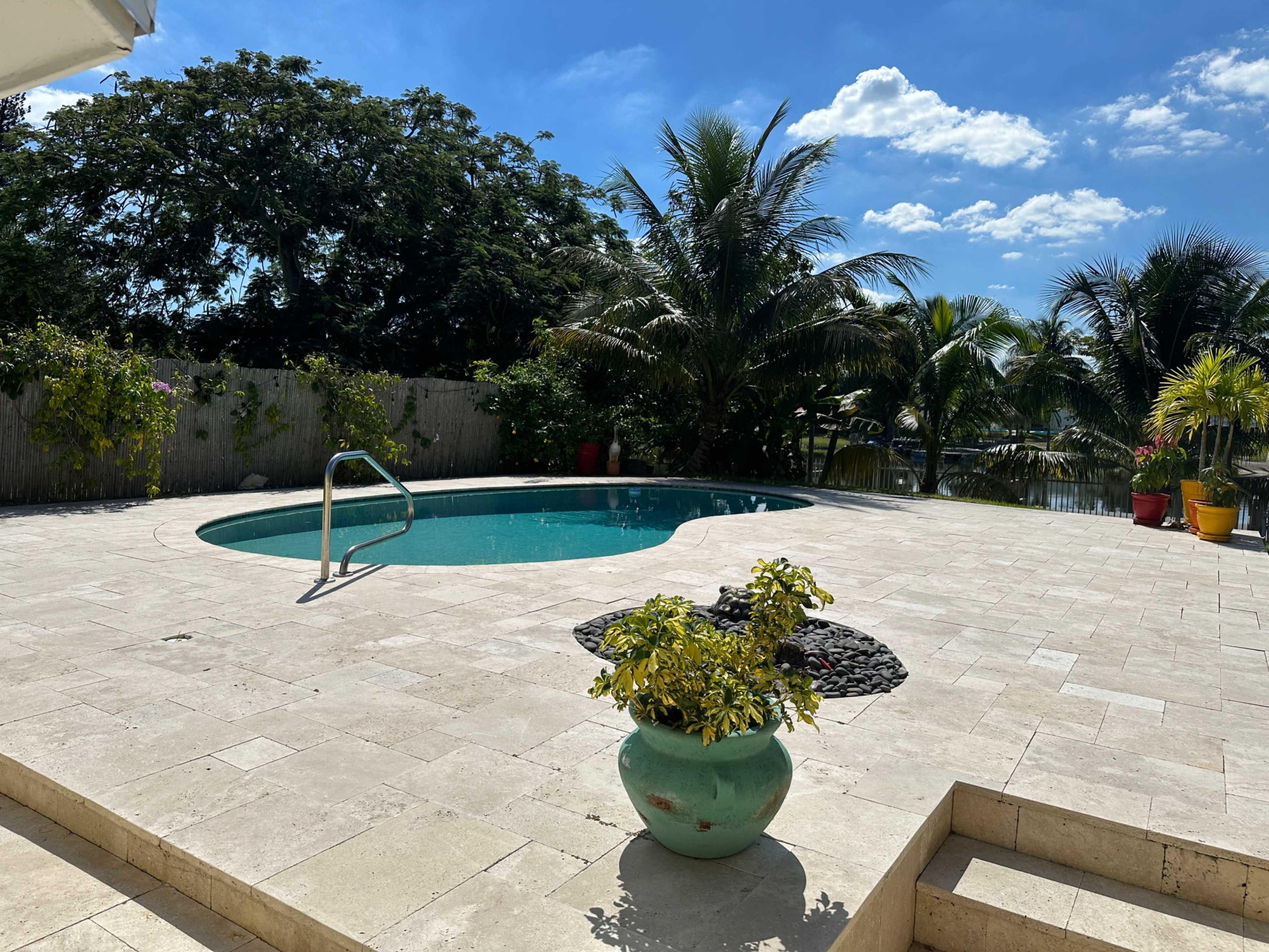 A circular swimming pool is surrounded by a stone patio and various potted plants under a clear blue sky.