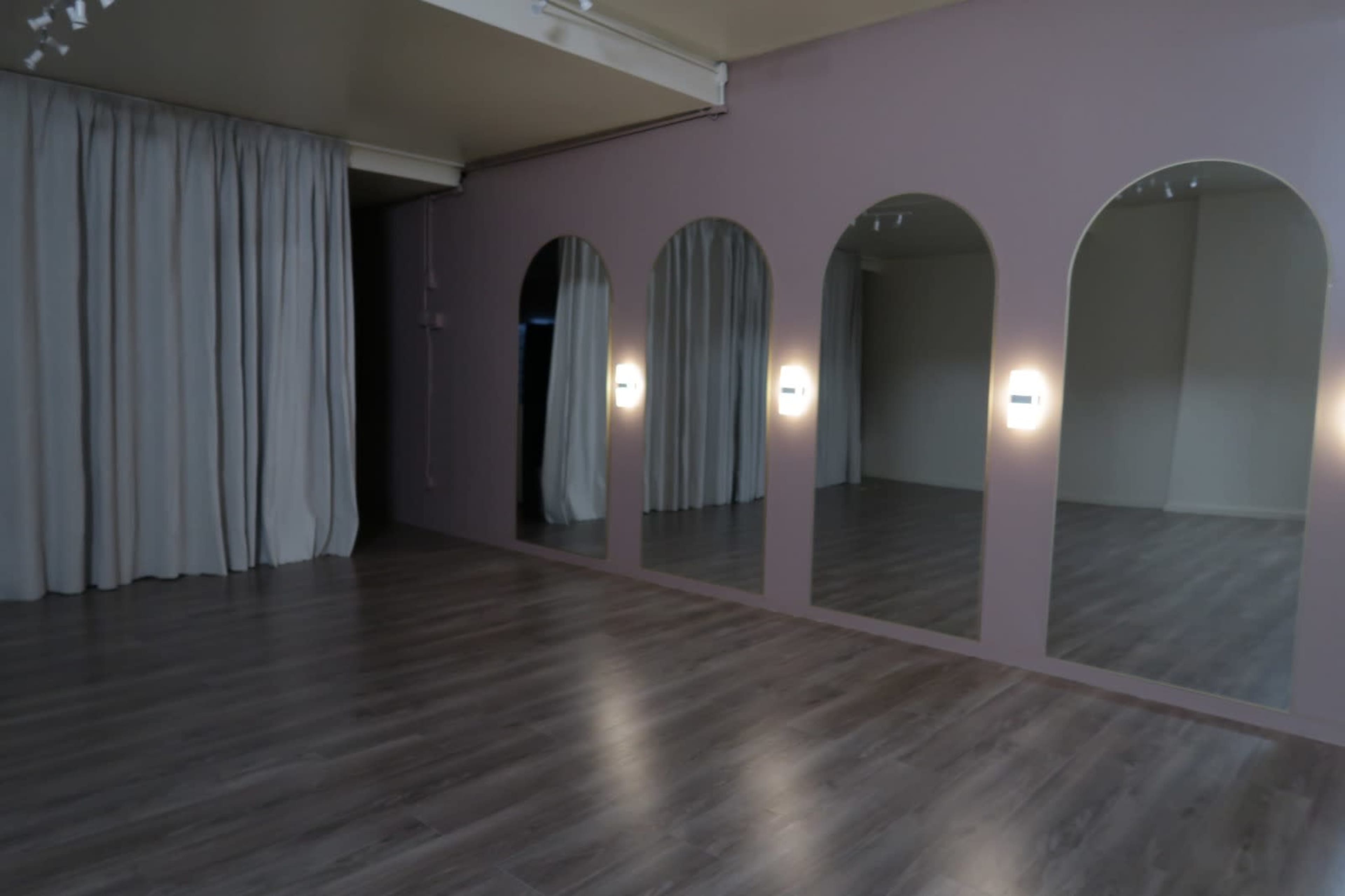 The image shows a room with a wooden floor, three arched mirrors on the wall, and gray curtains.