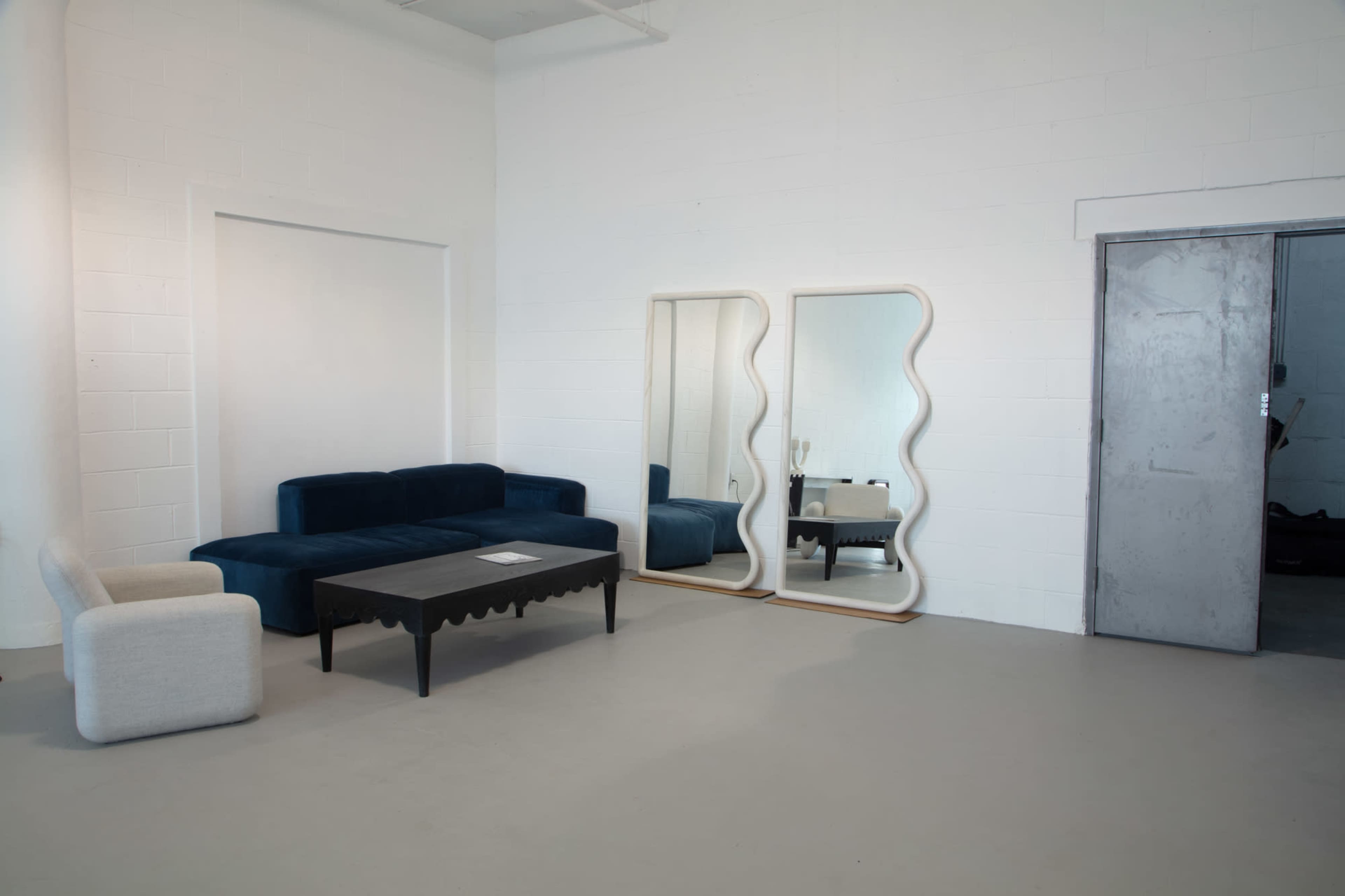A minimalist room features a blue sofa, a black table, and two large mirrors against a white wall.