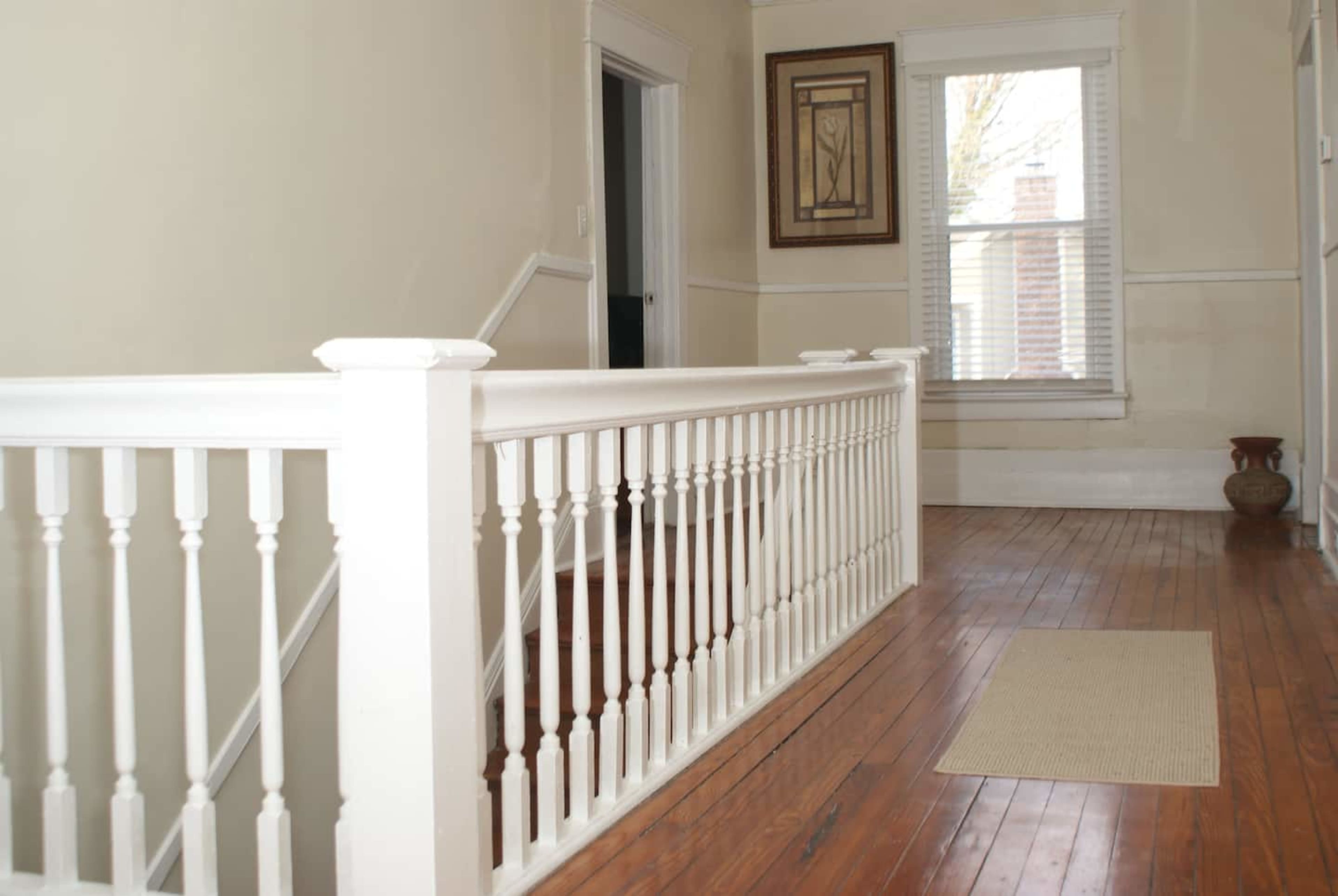 A hallway with a white wooden railing, wooden flooring, and a window allowing natural light.