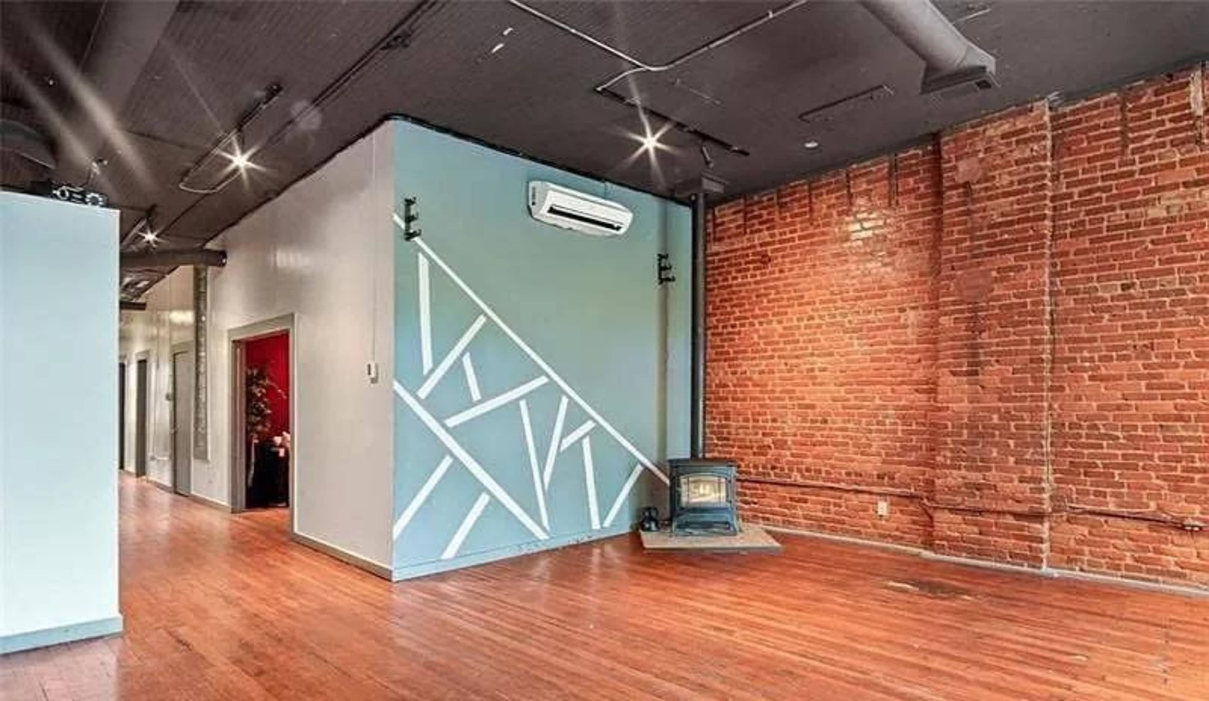 The image shows an interior space featuring exposed brick walls, a patterned accent wall, and a wood stove on a hardwood floor.