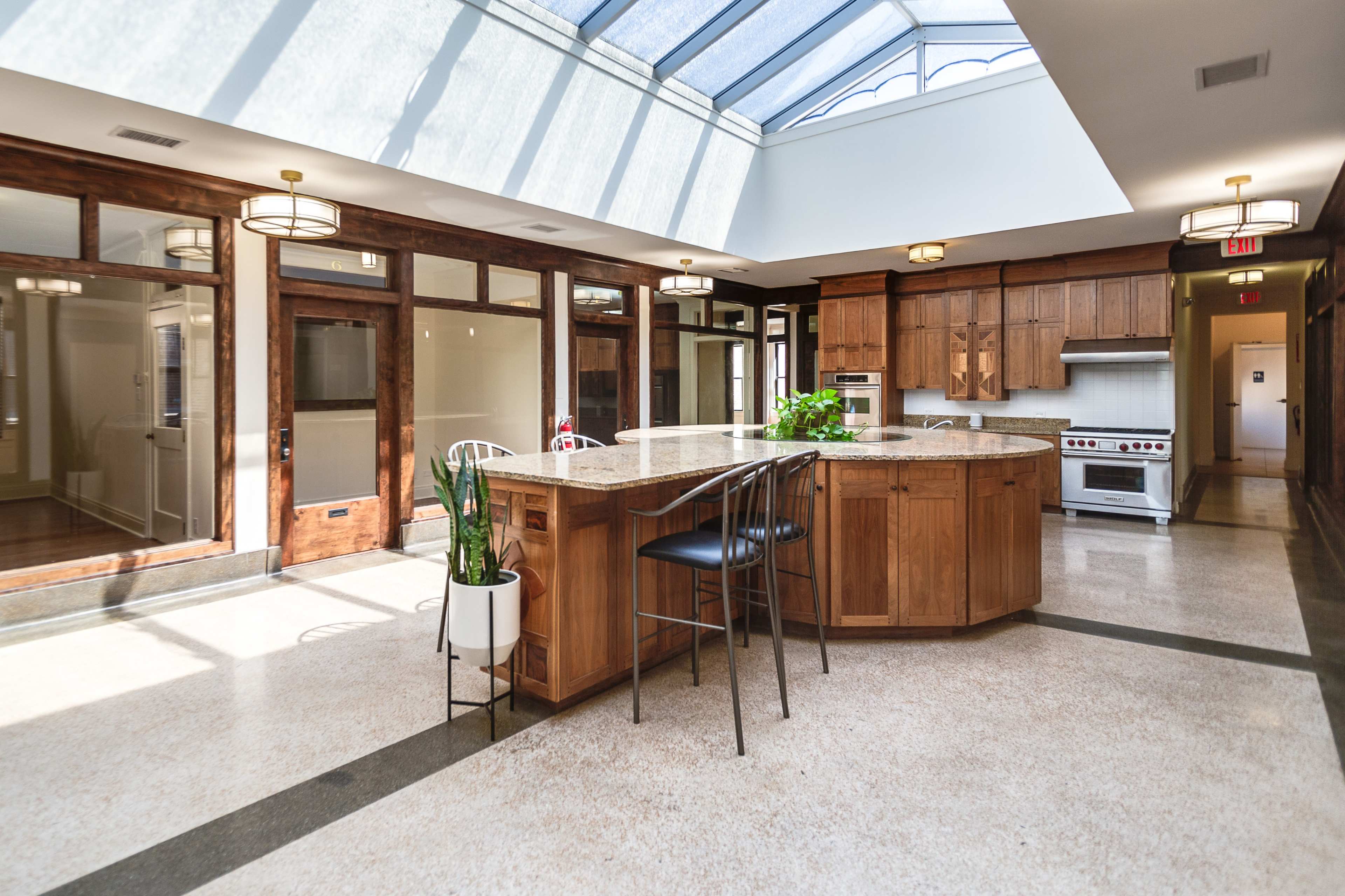 The kitchen features a large central island made of granite, surrounded by wooden cabinetry and illuminated by natural light from a skylight above.