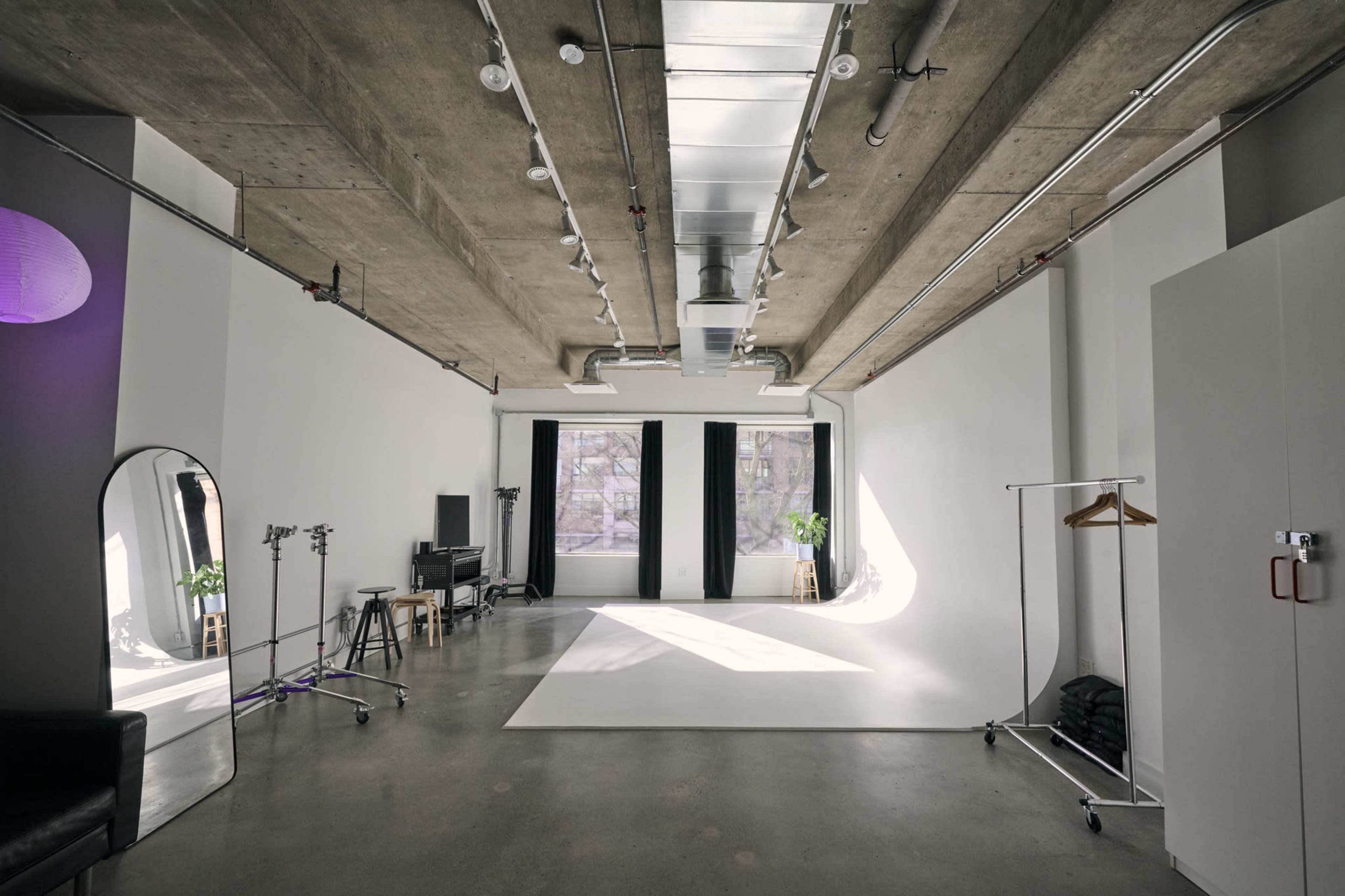 A spacious, modern studio features large windows, minimalist decor, and soft natural lighting.