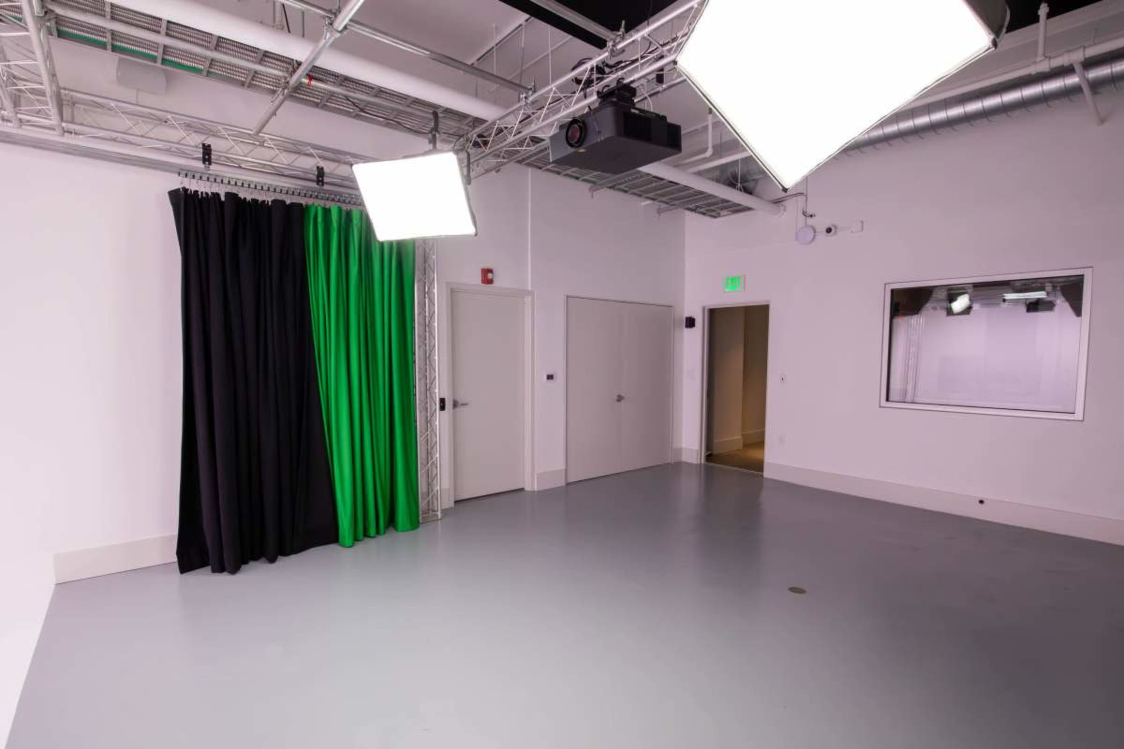 The image shows an empty studio space featuring a green backdrop, black curtains, and overhead lighting in a minimalist layout.
