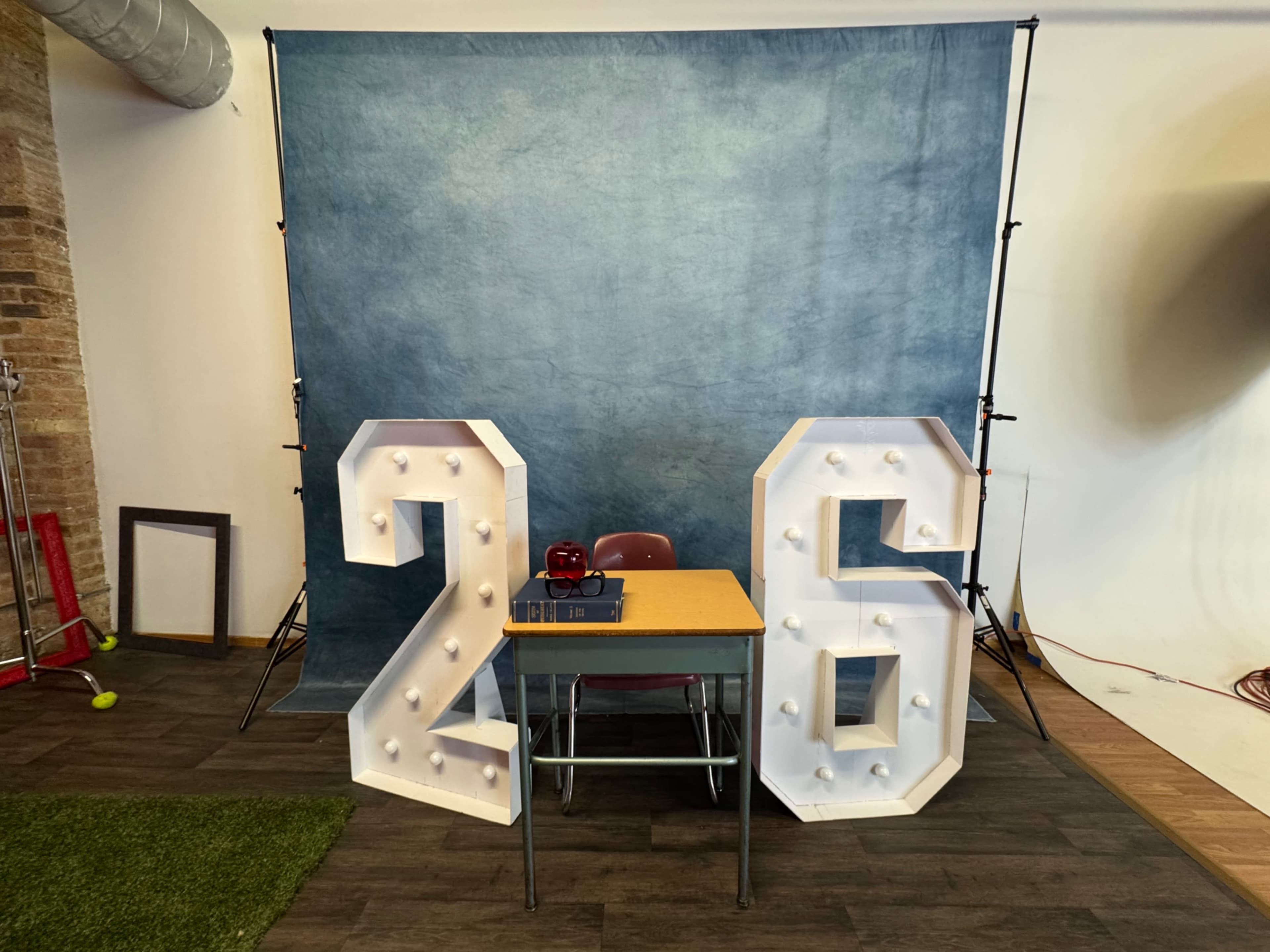 The image shows a large "26" marquee display with lights positioned in front of a table and a blue backdrop in a studio setting.
