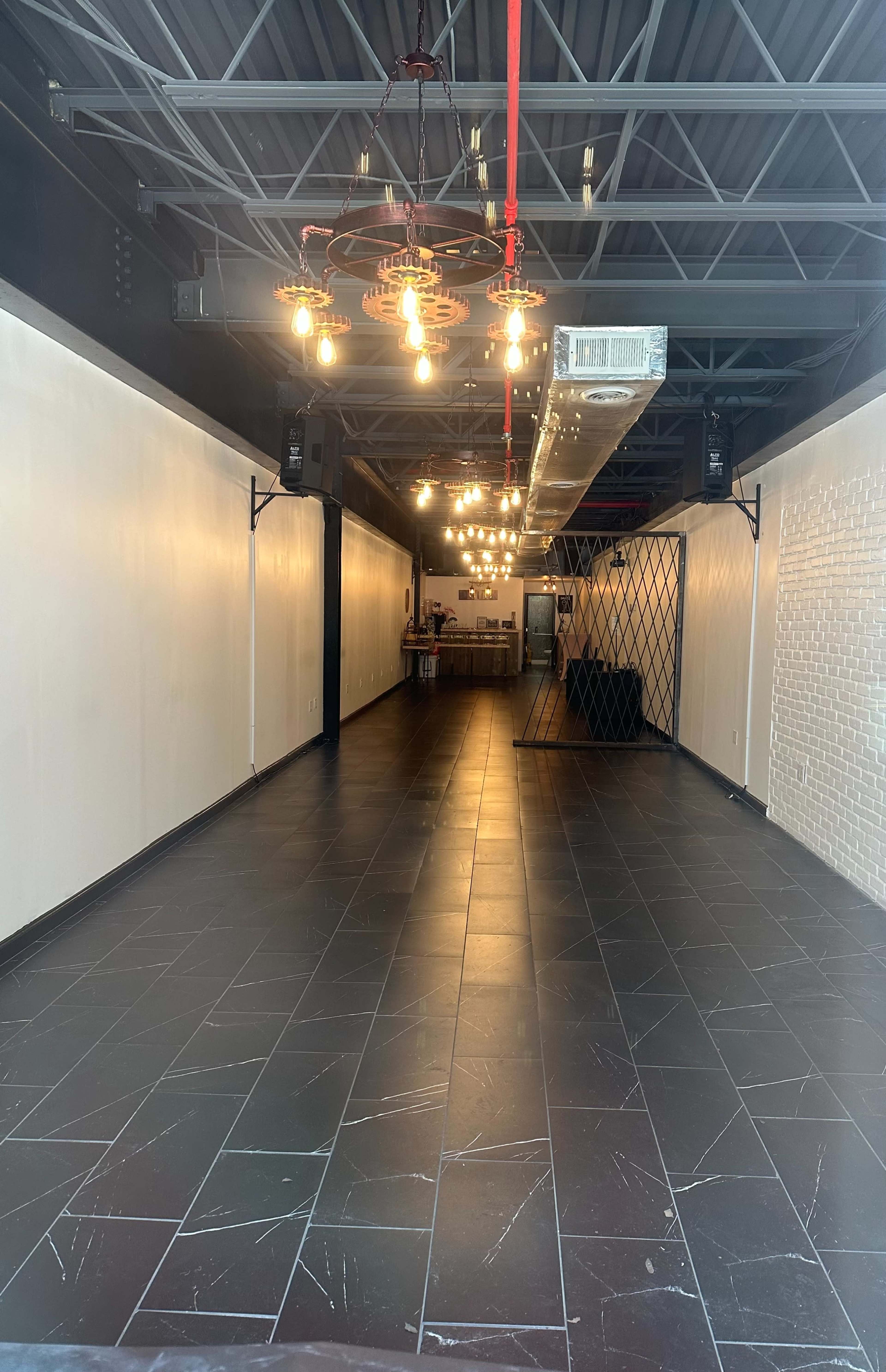 A spacious, empty interior with dark tile flooring, exposed lighting fixtures, and a long hallway leading to a counter area at the far end.