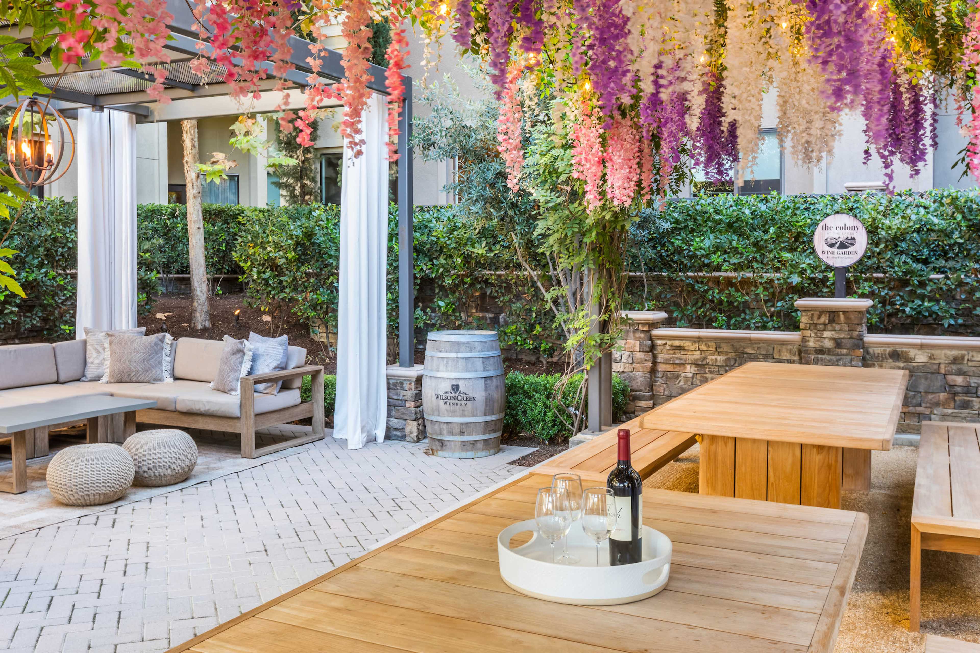 A patio area features wooden tables and seating, decorated with hanging floral arrangements and a wine bottle with glasses on a tray.