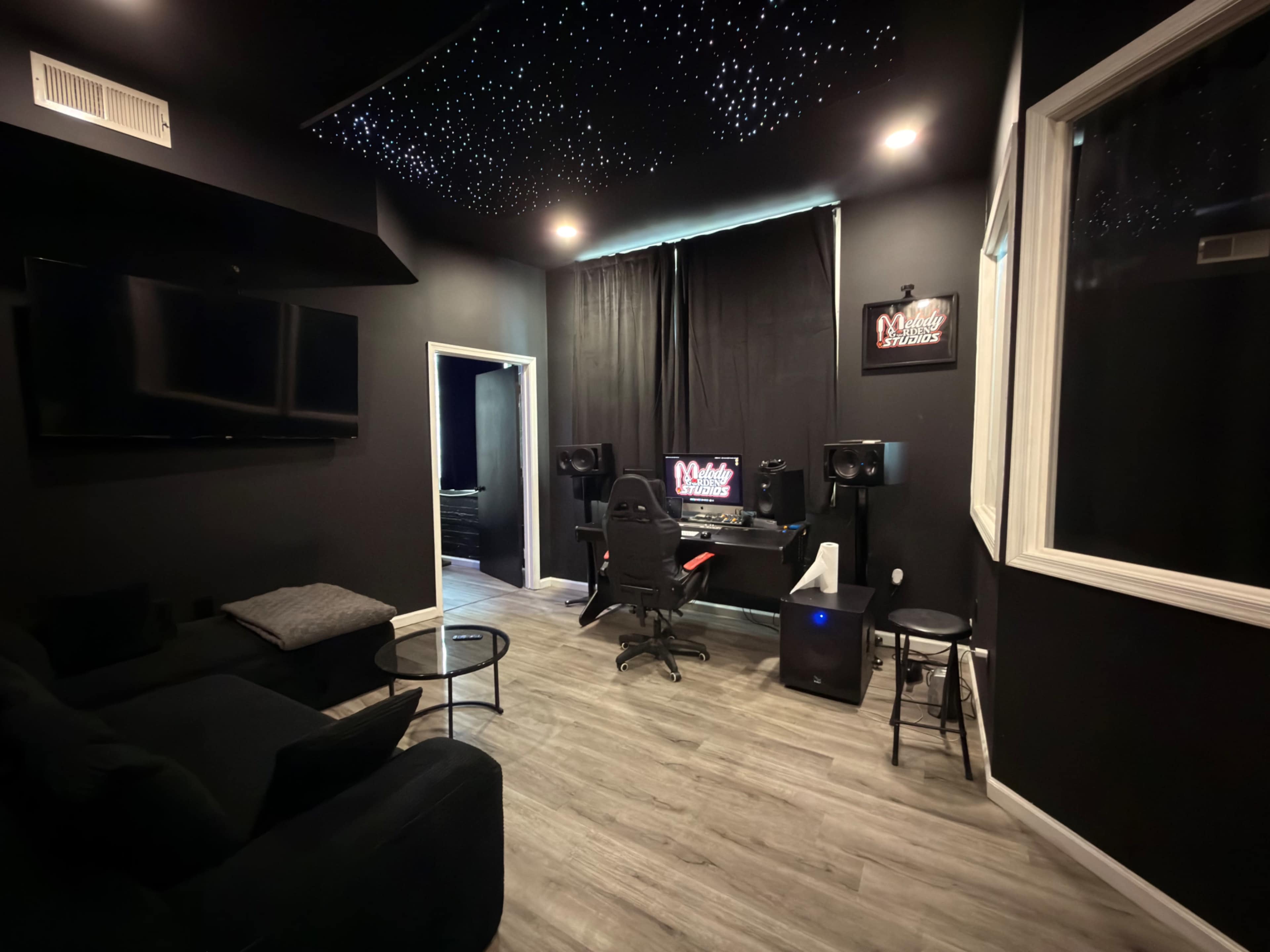 The image shows a modern recording studio featuring a desk with a computer, audio monitors, and a gaming chair, all set against a dark, starry ceiling backdrop.
