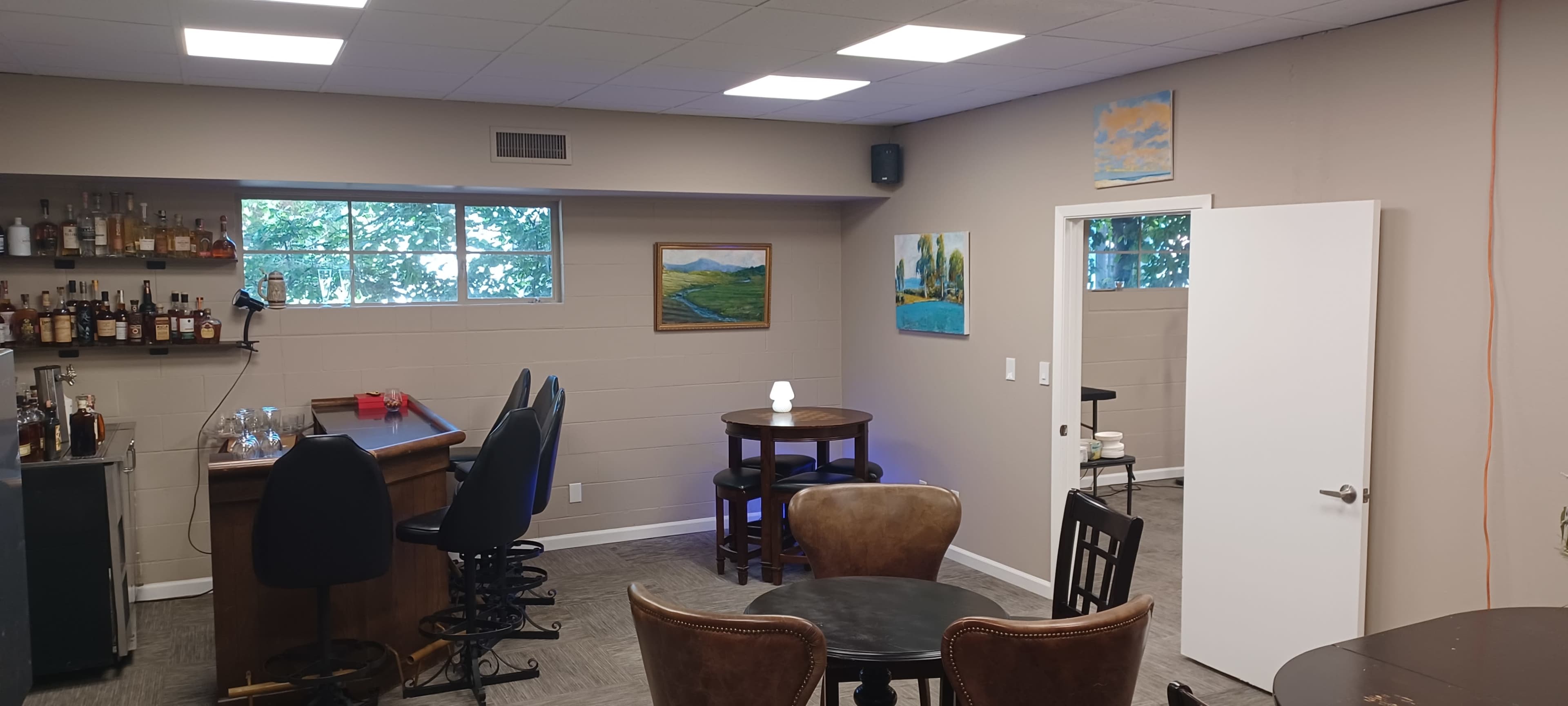 The image shows a modern, well-lit lounge area featuring a bar, tables, and artwork on the walls.