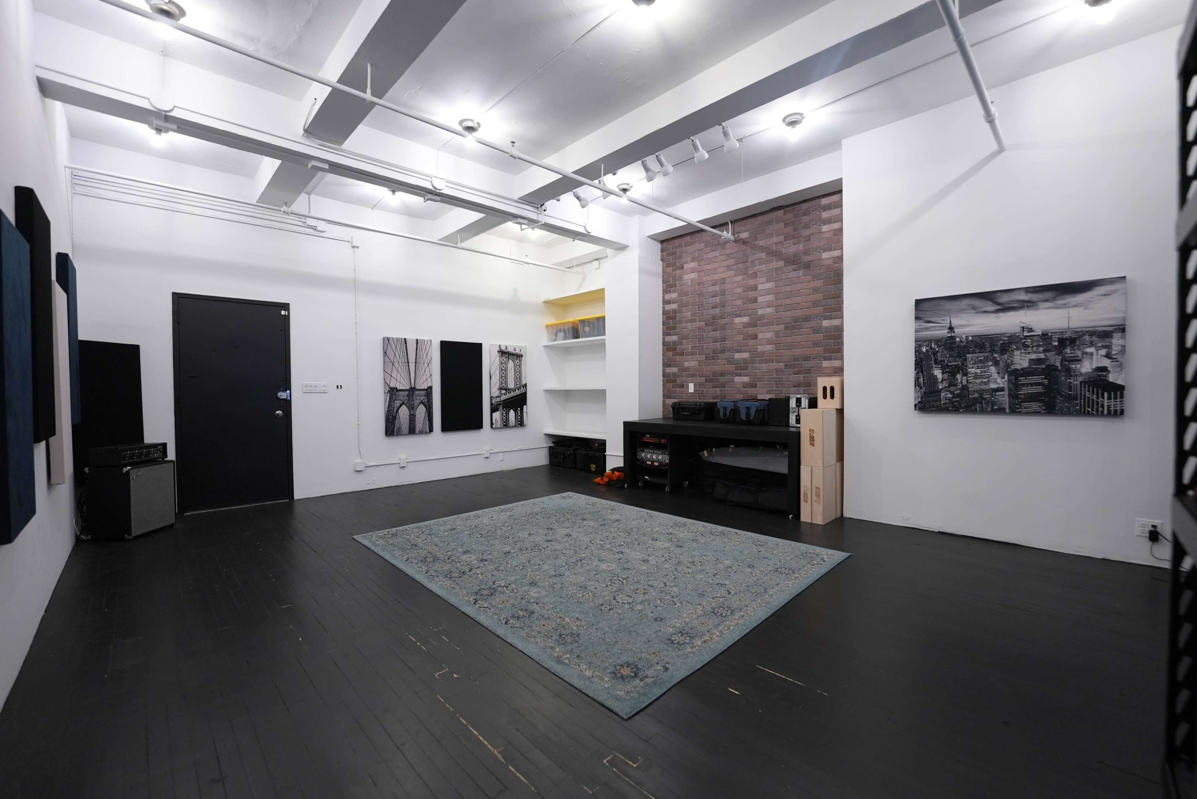 A spacious, minimalist gallery-style room with a dark wooden floor and a large area rug, featuring white walls and various wall-mounted artwork.