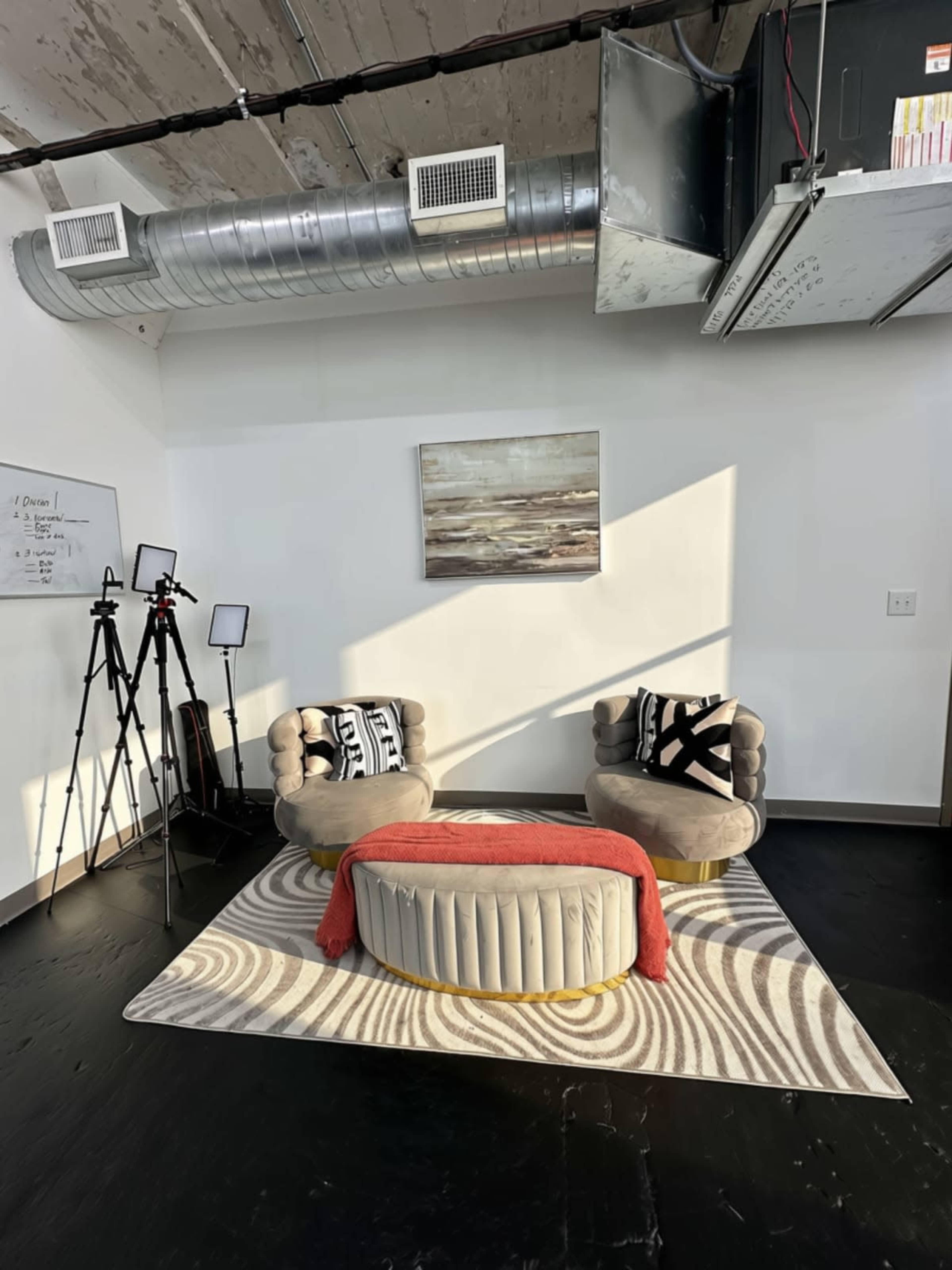 The image shows a modern sitting area featuring two patterned chairs and an oval coffee table, with floor lamps and a wall art piece in a well-lit space.